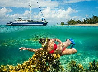 Snorkeler over a reef beside an anchored catamaran