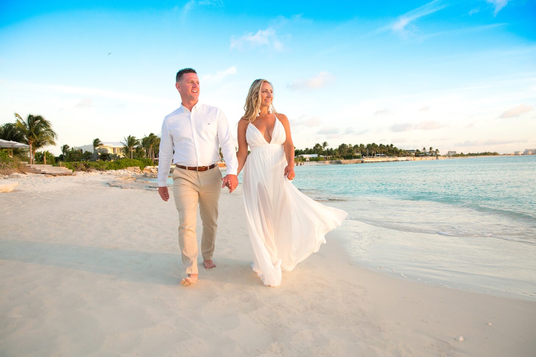 Couple walking hand in hand along a turquoise shoreline at sunset
