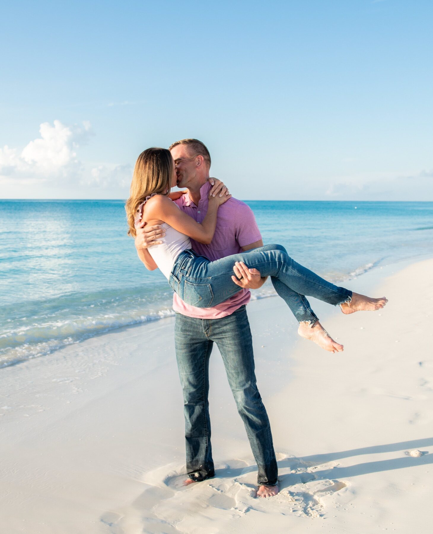 Man carrying his laughing partner while they kiss at the water's edge