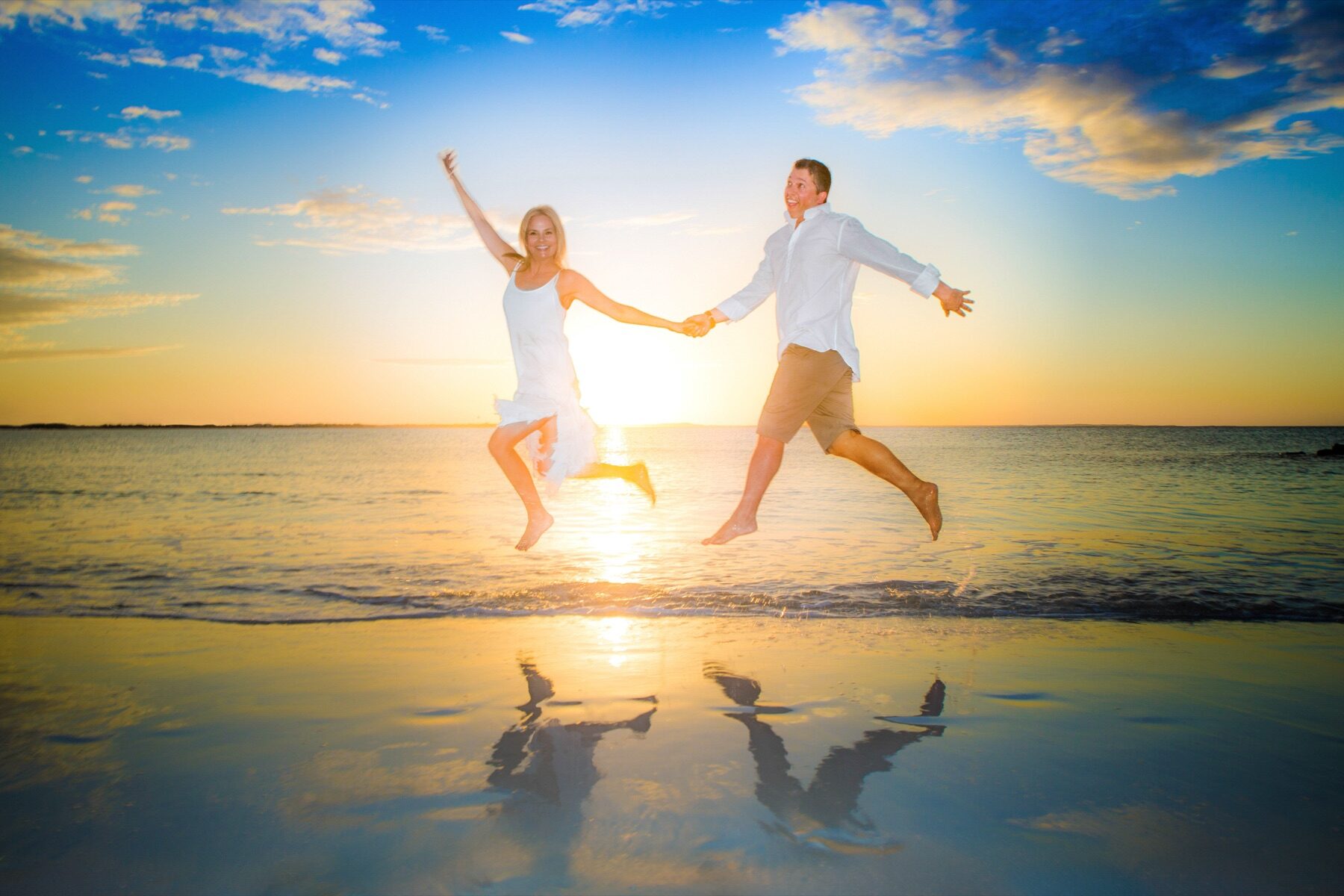 Couple leaping hand in hand on the beach at golden sunset, reflections in wet sand