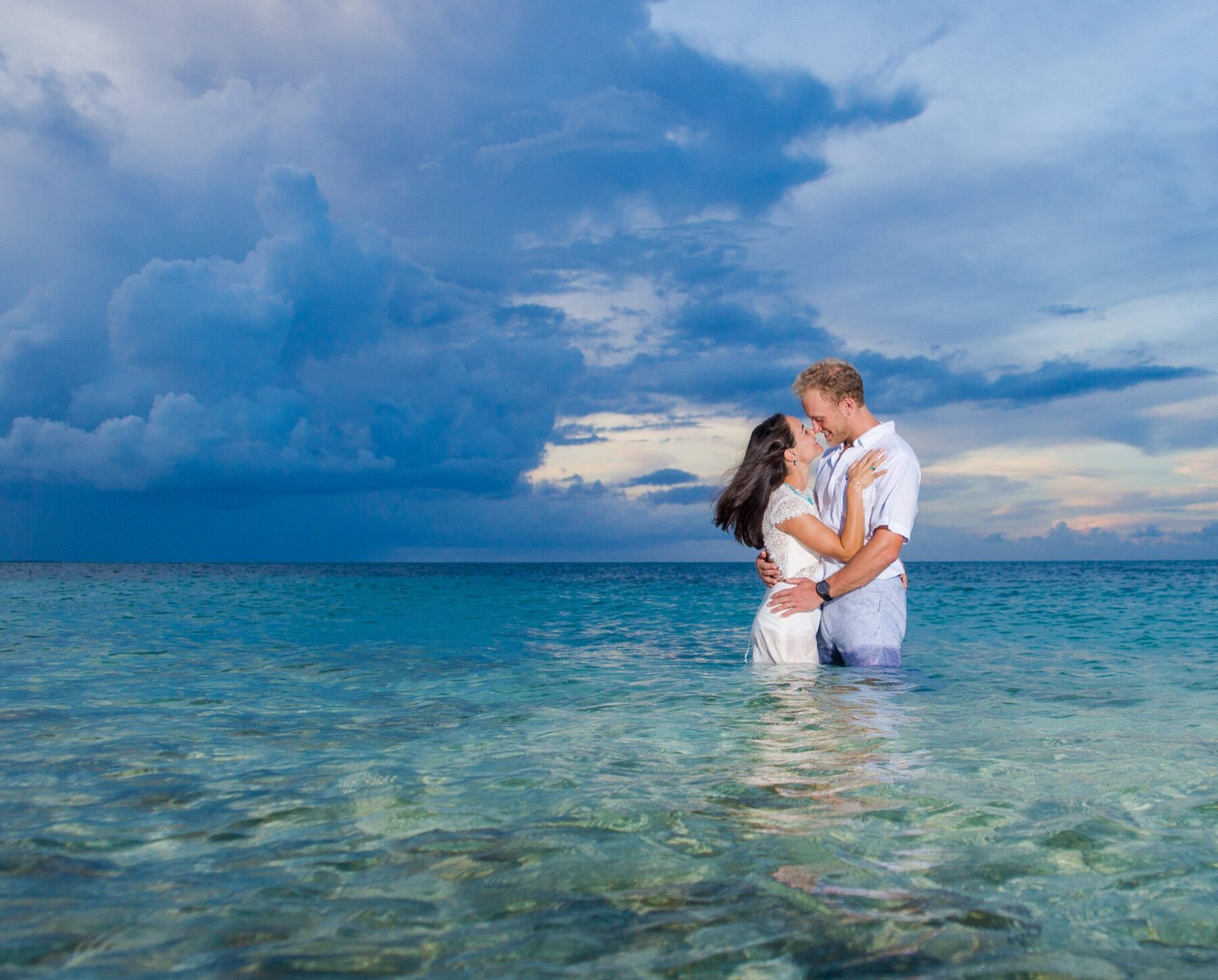 Couple embracing waist deep in calm turquoise water under a cloudy sky