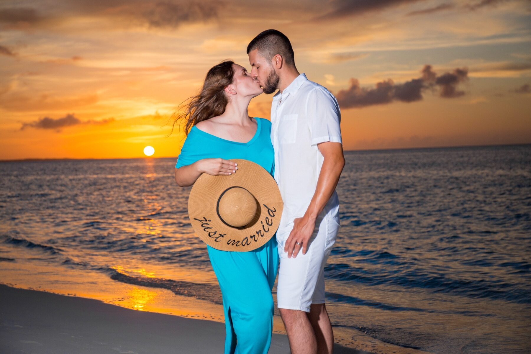 Couple kissing at sunset, woman holding a straw hat that reads just married