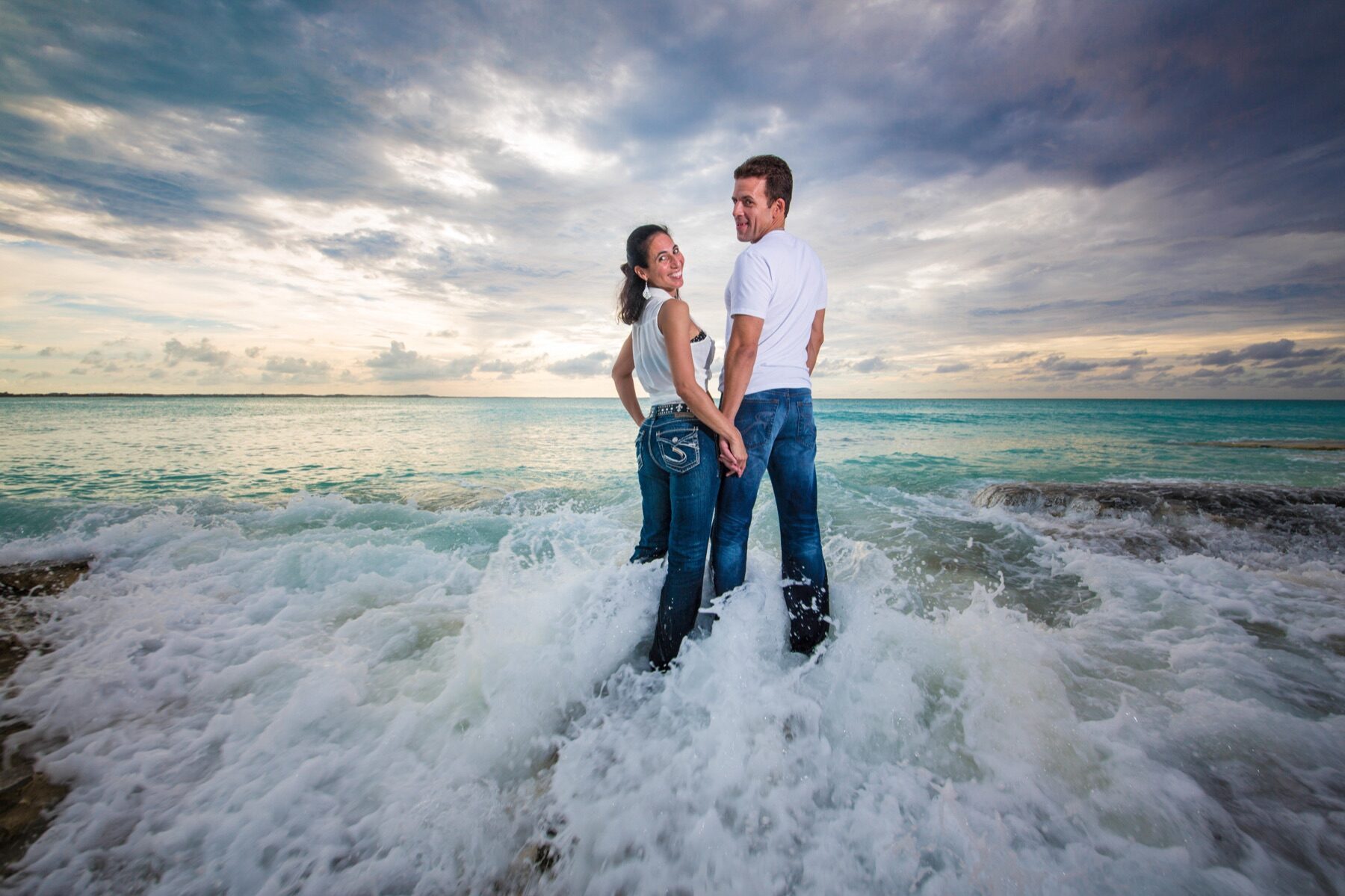 Couple holding hands and glancing back while standing in crashing surf