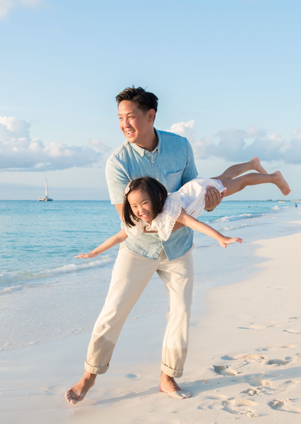 Father holding his daughter in an airplane pose along the shoreline