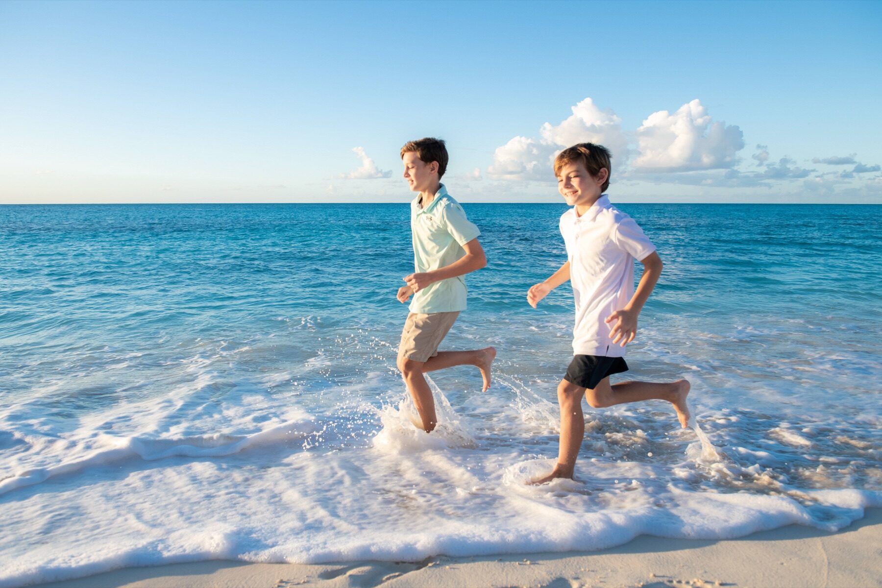 Two boys running through the shallow surf splashing water