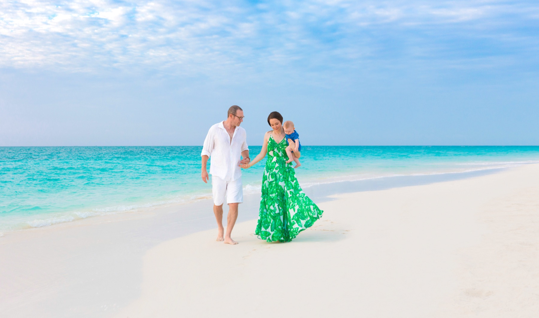 Parents holding hands on a Turks and Caicos beach, mother carrying a baby