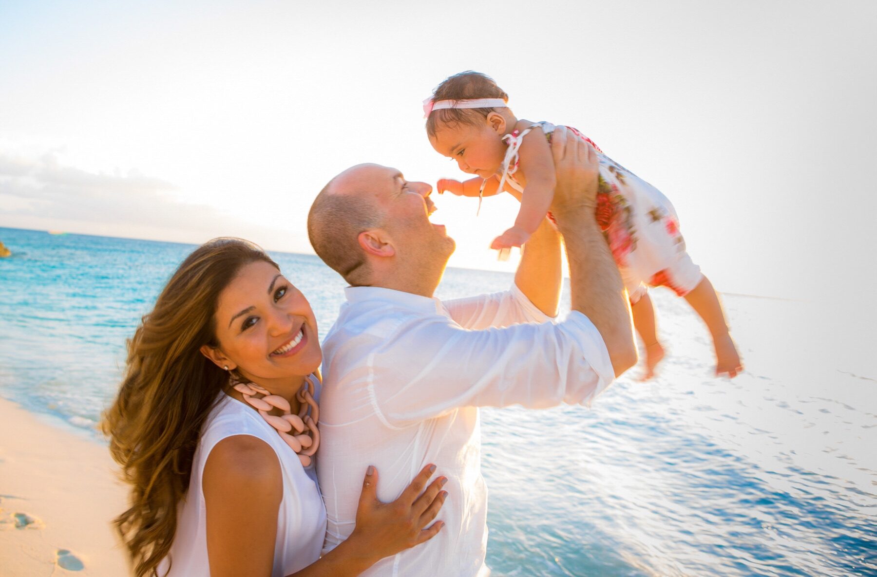 Father lifting his giggling baby into the air by the water at golden hour