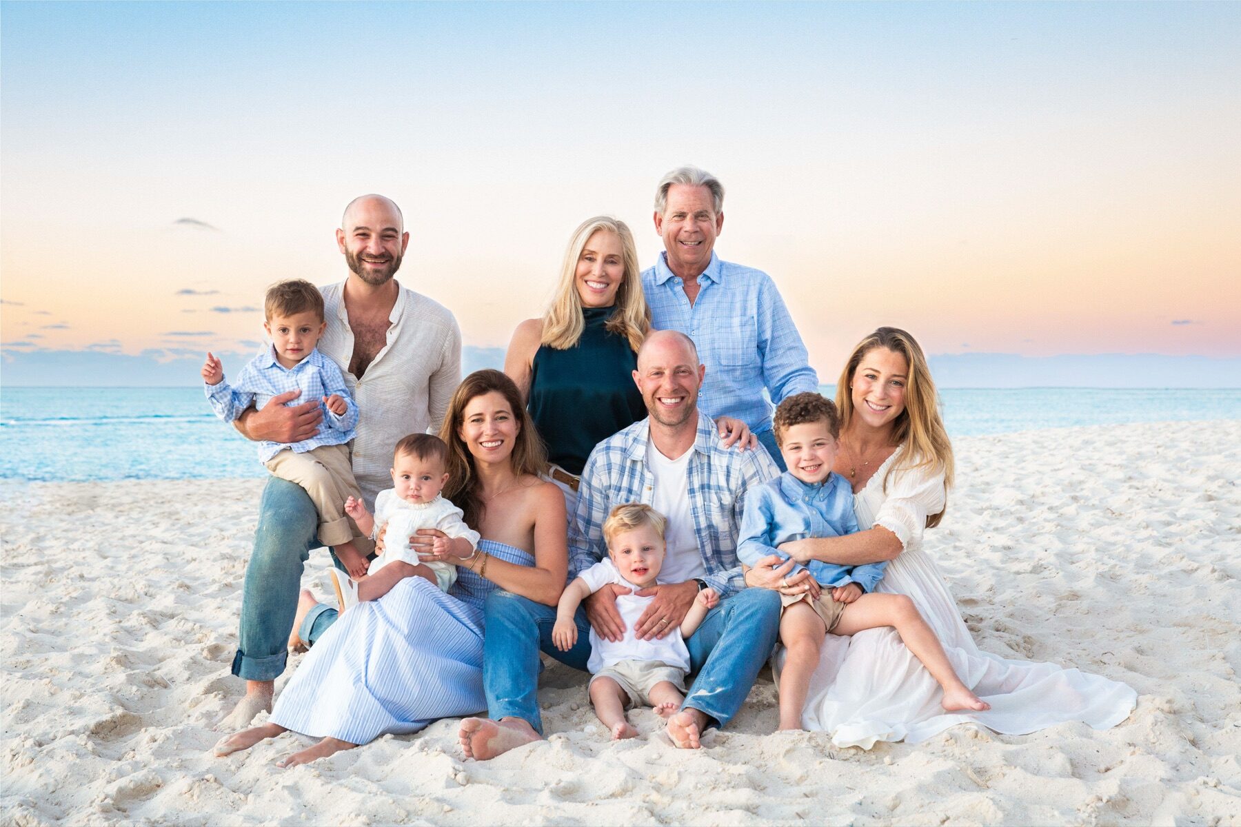 Multigenerational family of ten seated together on the sand at dusk