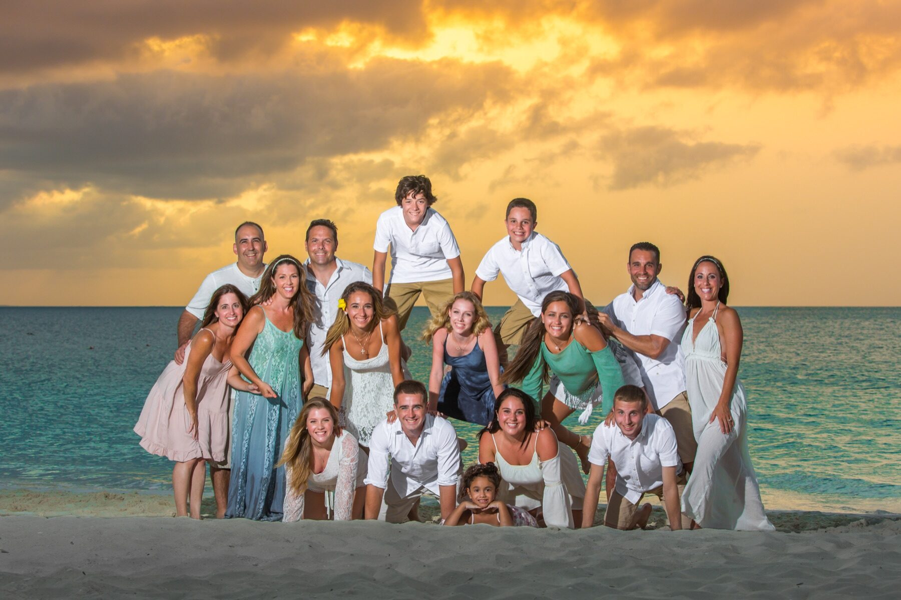 Large extended family piled together in a pyramid pose on the beach under a golden sky
