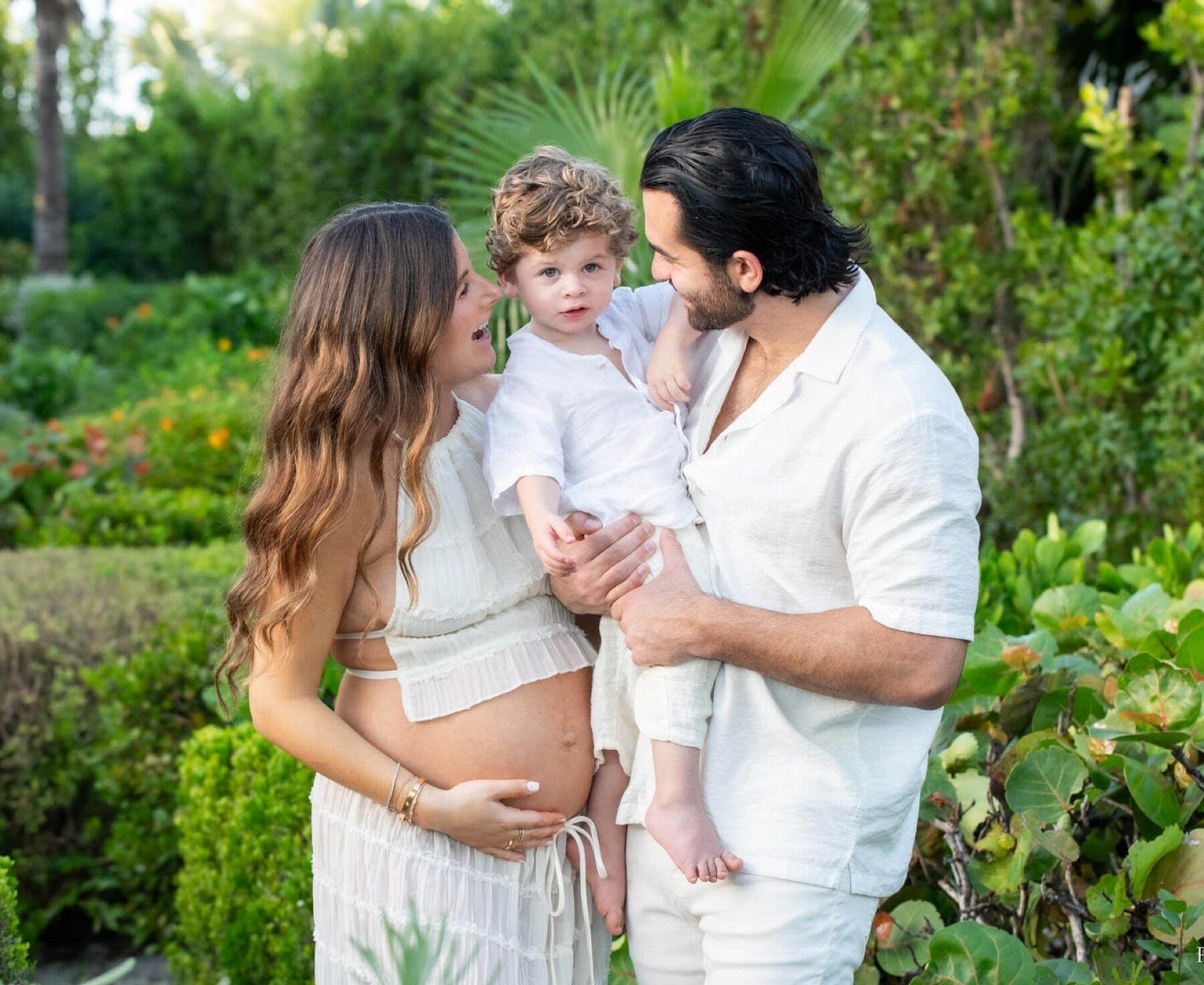 Pregnant mother and father smiling at their toddler in a Turks and Caicos garden