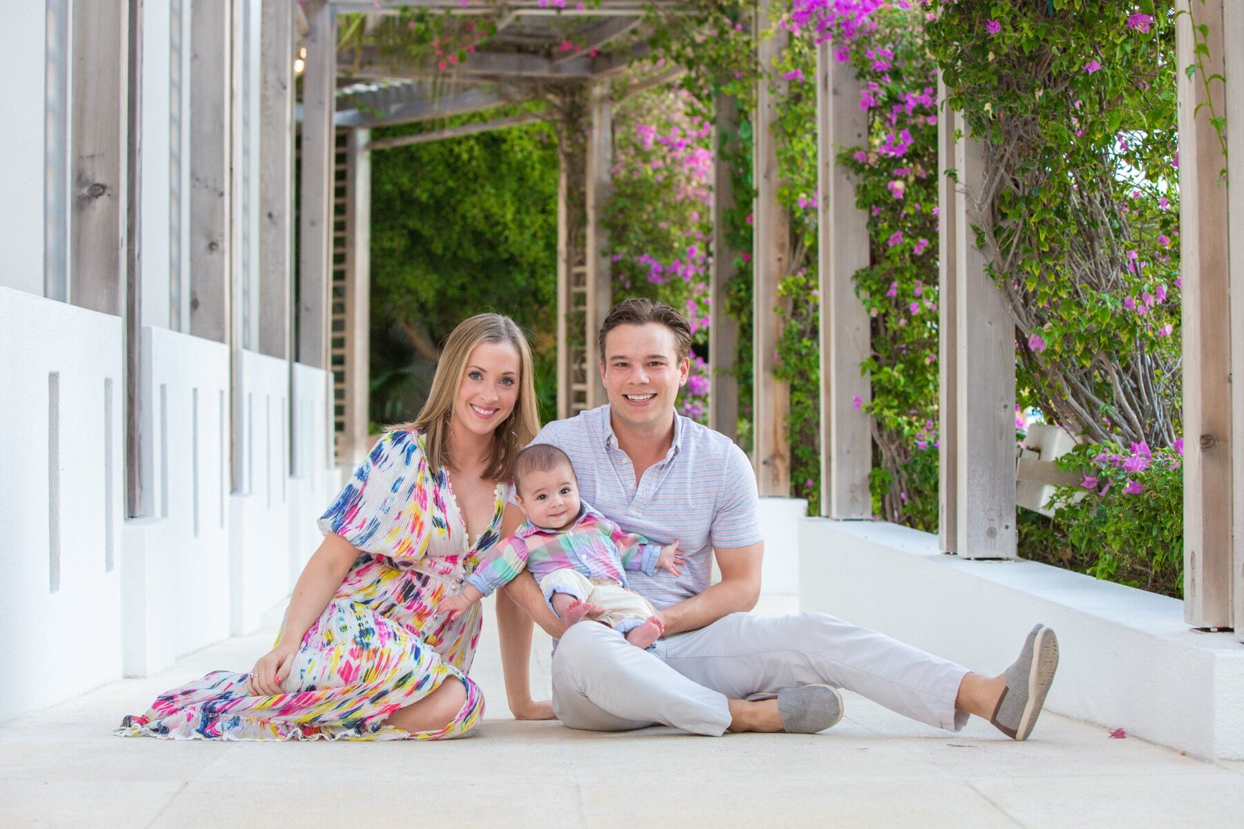 Young couple sitting on a tiled walkway holding their baby among bougainvillea