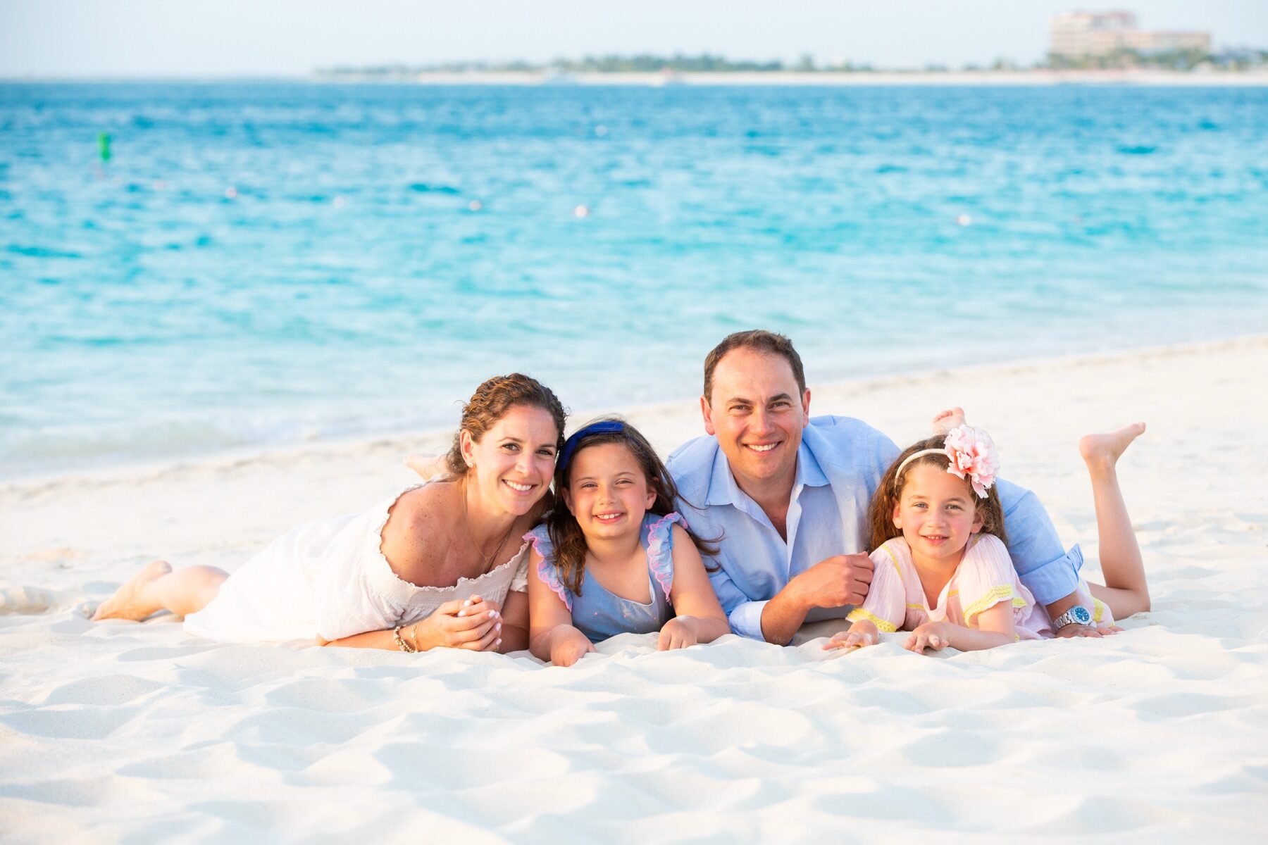 Family of four lying together in the sand, two young daughters between their parents