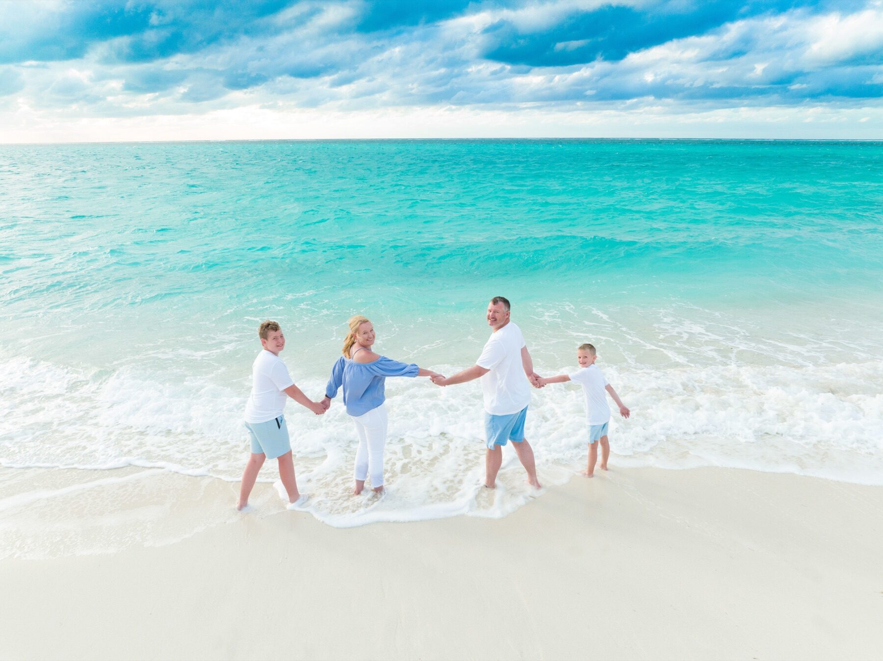 Family of four holding hands in a line in the shallow surf