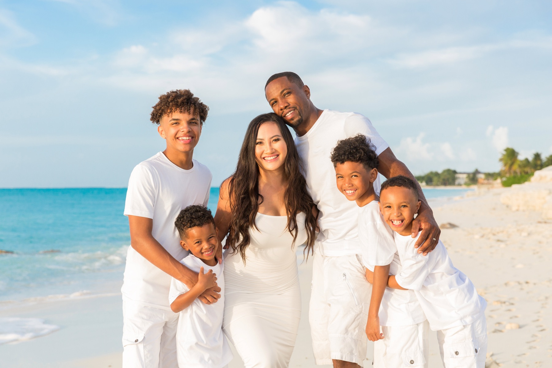Family of six in matching white outfits smiling together on the beach