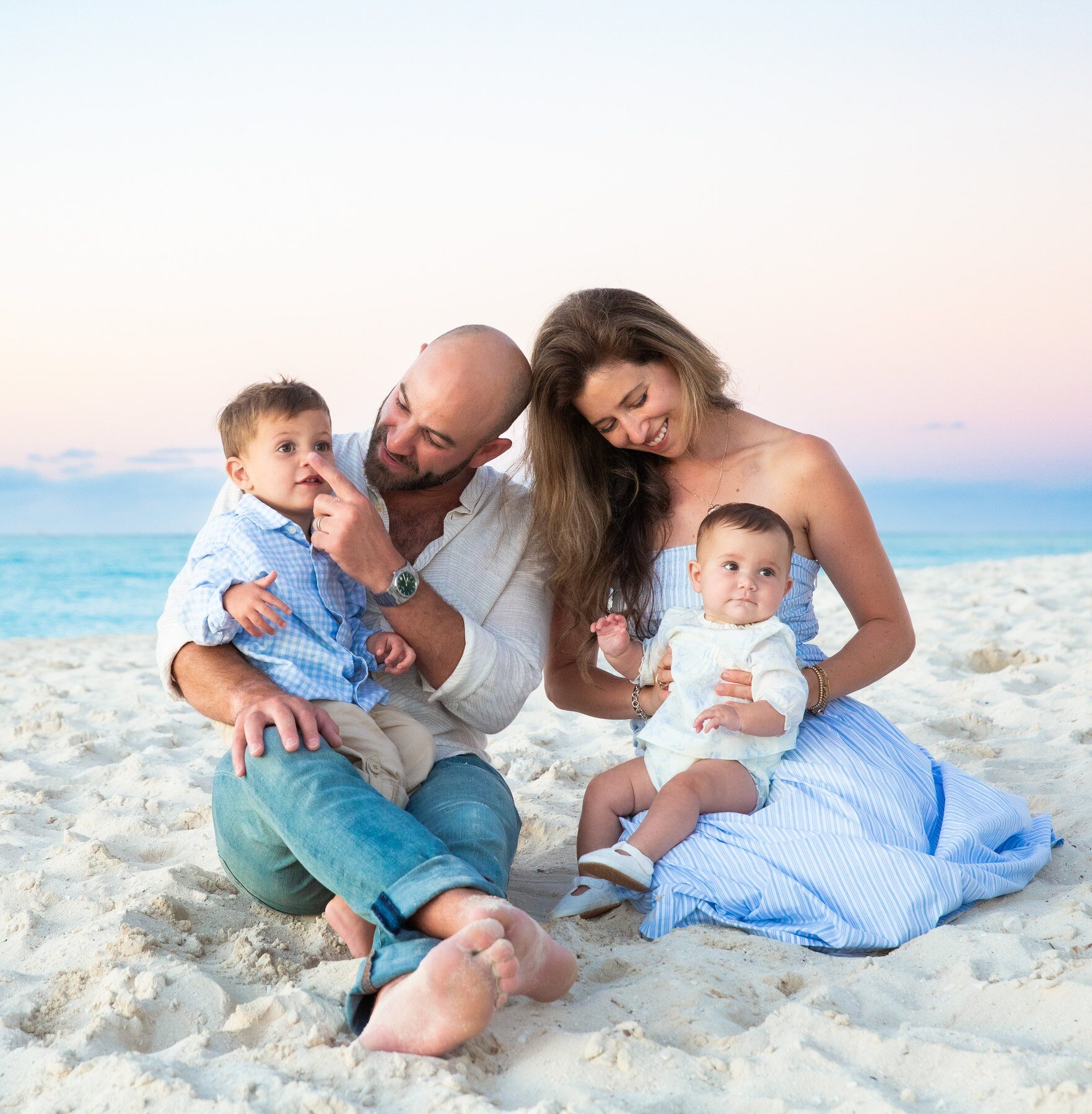 Parents sitting in the sand with two toddlers at dusk in Turks and Caicos