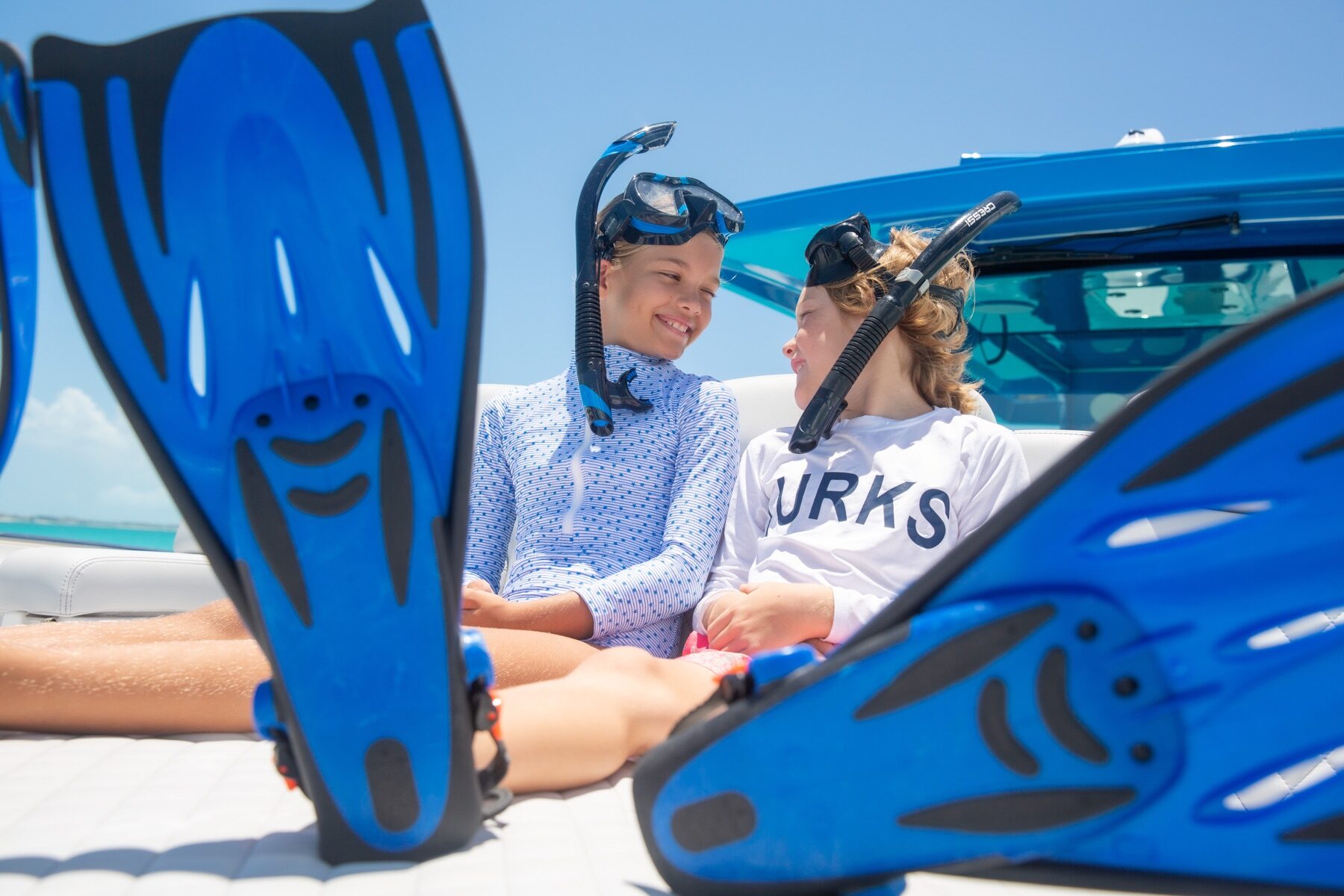Two children in snorkel masks and fins sitting together on a boat