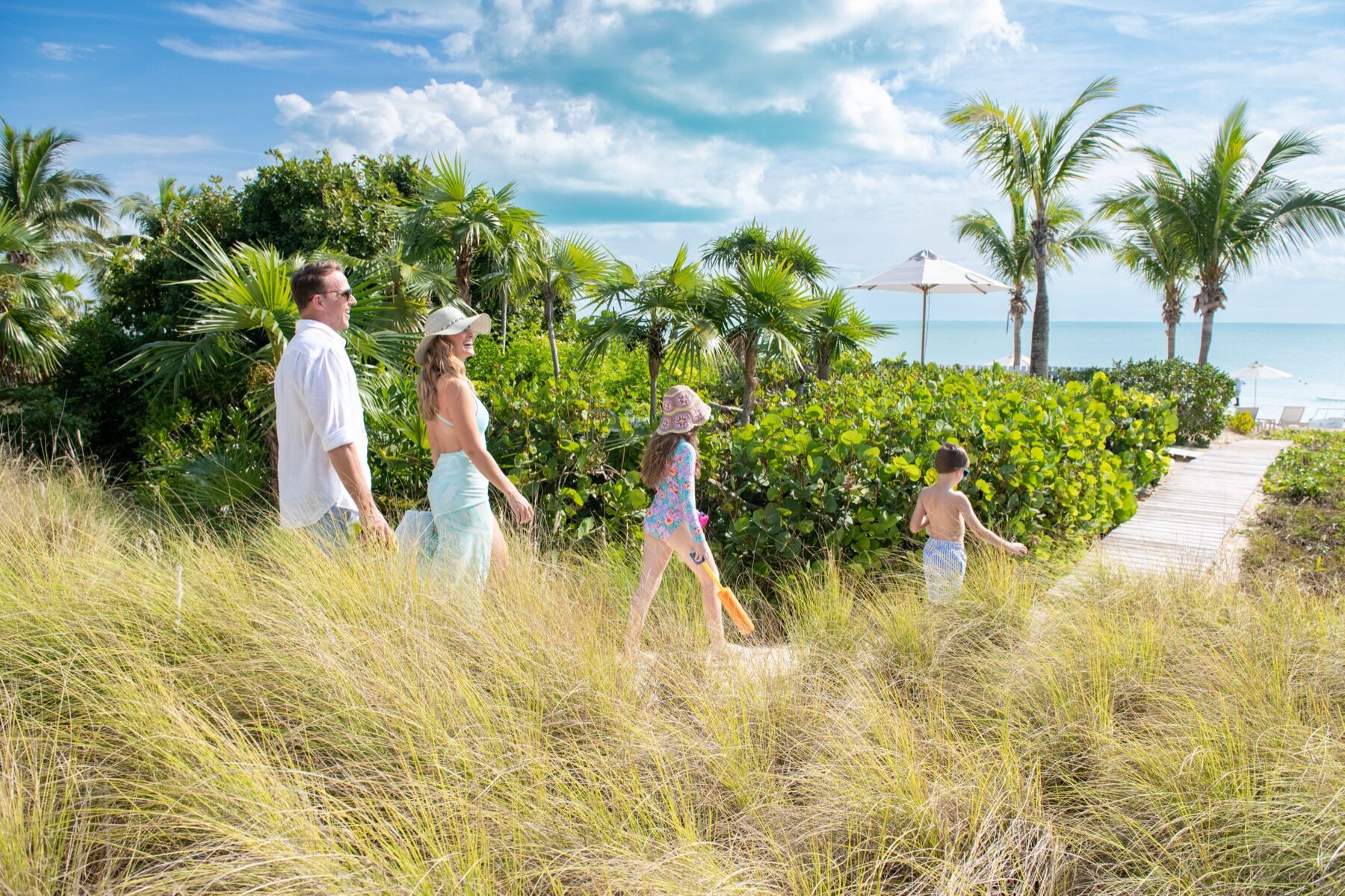 Family of four strolling through tall dune grass toward the shore