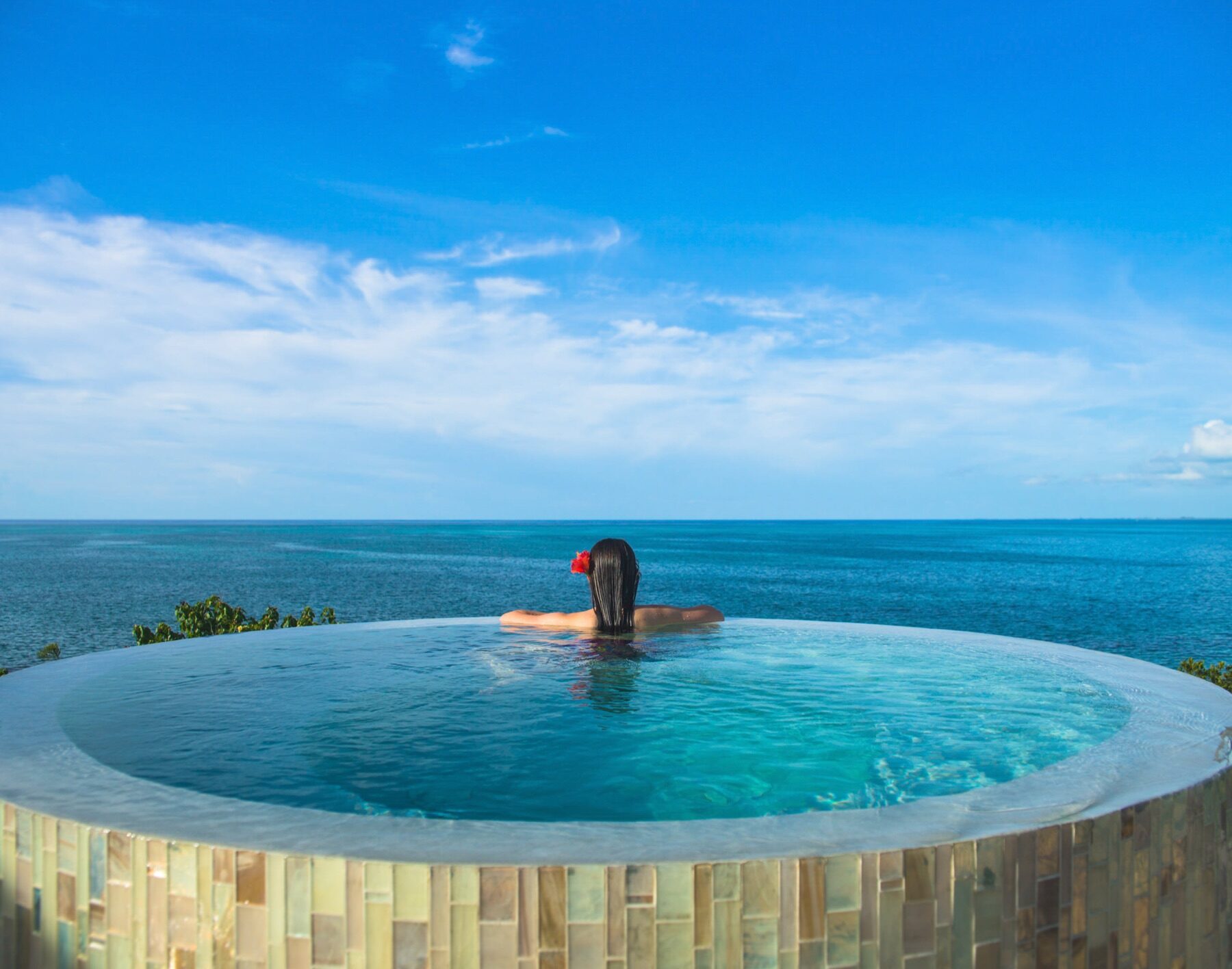 Woman resting her arms on the edge of a round infinity pool at sea