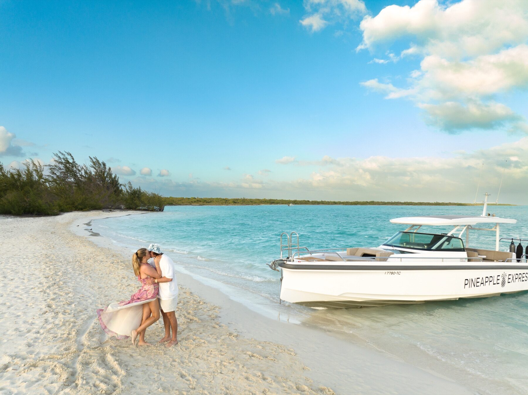 Couple embracing on the sand beside a docked boat named Pineapple Express