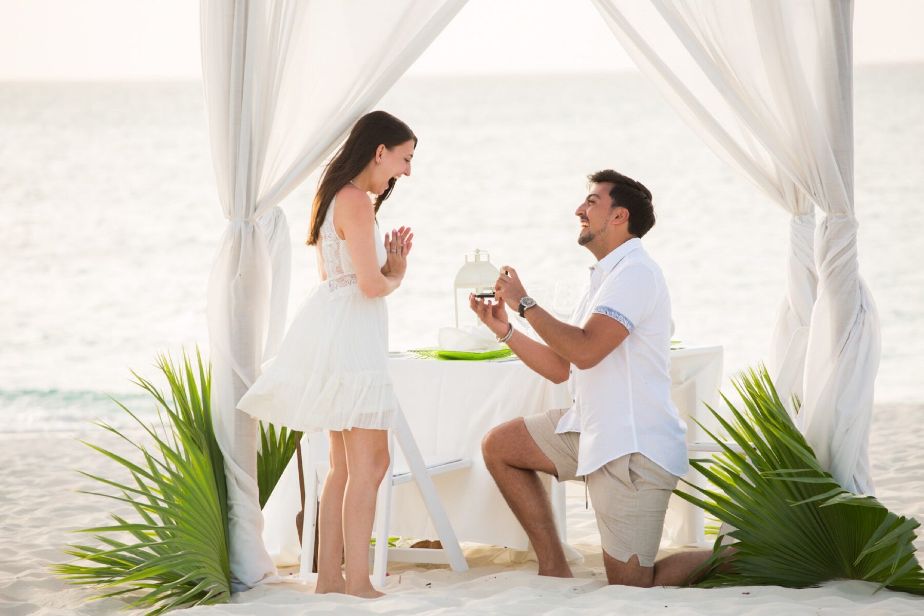 Man proposing beneath a draped canopy set for dinner on a Turks and Caicos beach