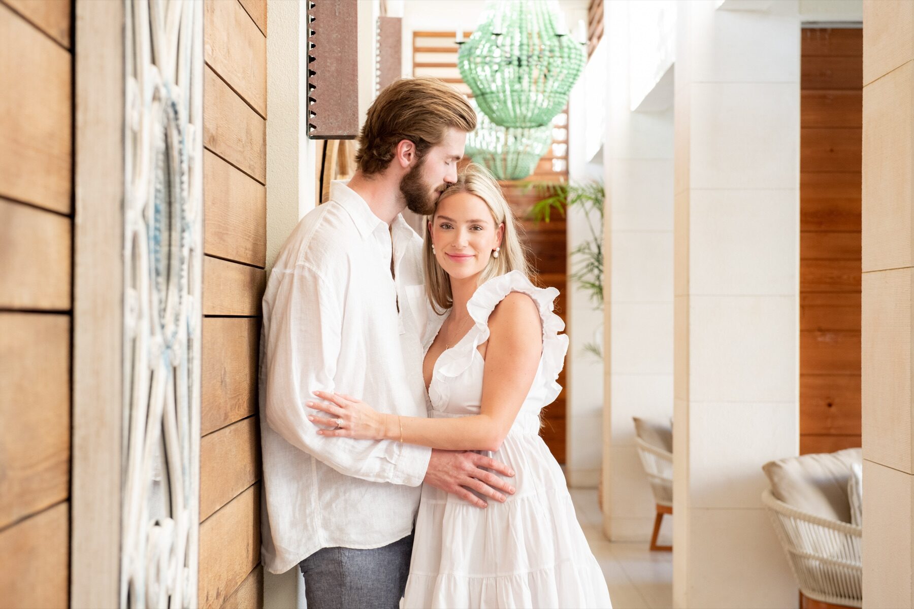 Newly engaged couple embracing in a sunlit hallway decorated with a green pendant lamp