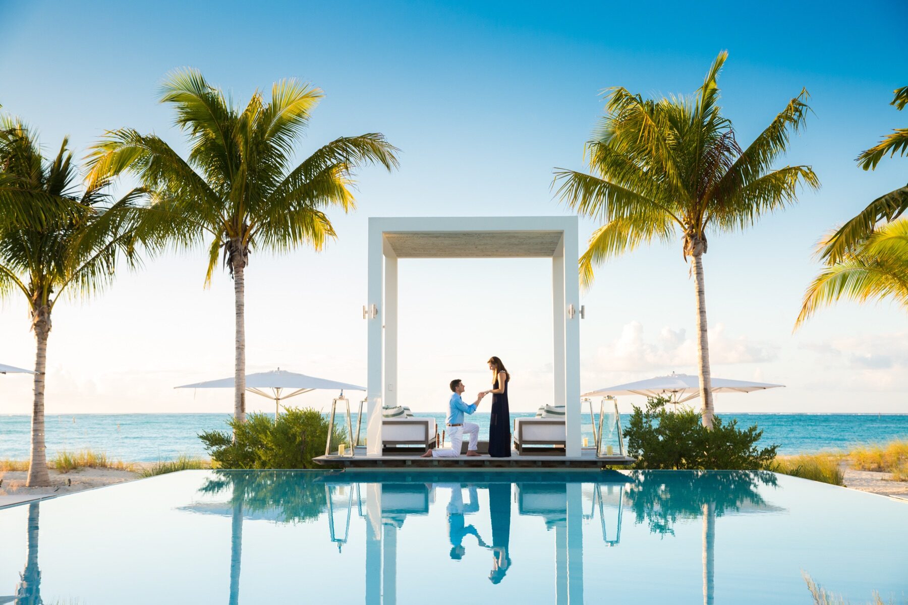 Man proposing under a white cabana reflected in an infinity pool at sunrise