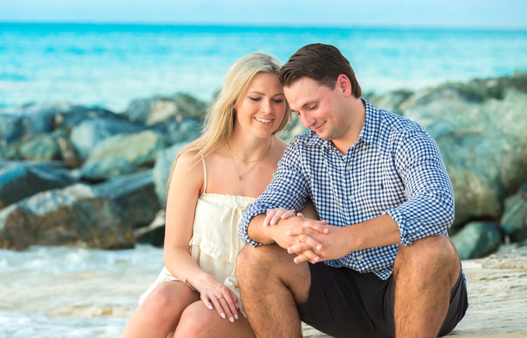 Couple sitting on a jetty of rocks holding hands and looking down at a new ring