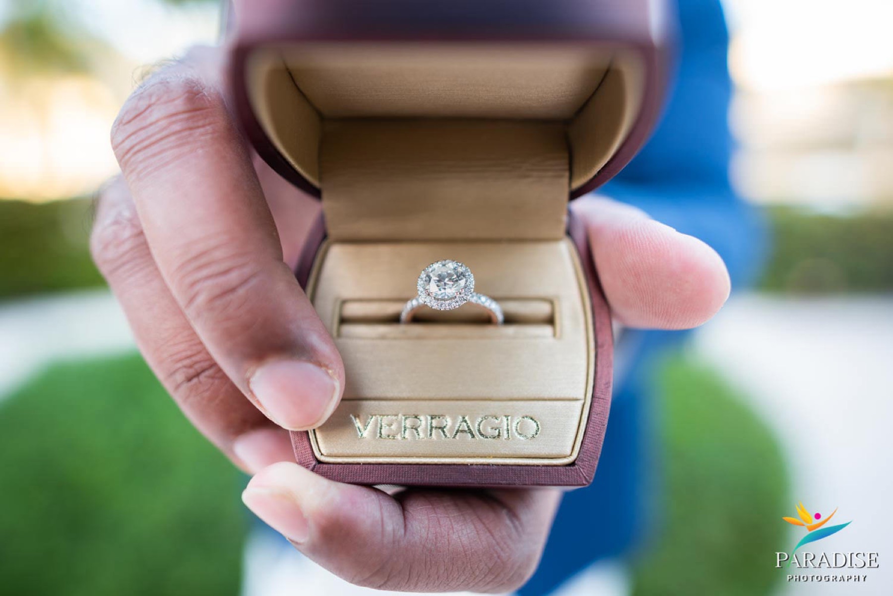 Close-up of a hand presenting an open ring box with a diamond engagement ring