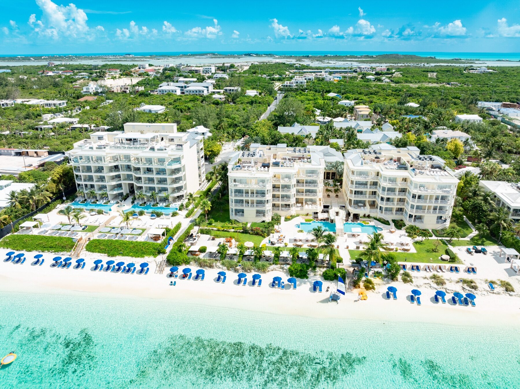 Aerial view of a beachfront resort with pools and rows of lounge chairs