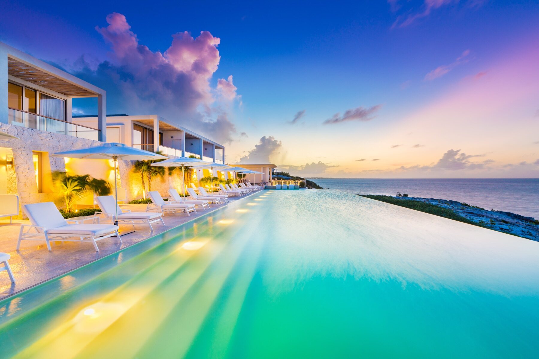 Resort infinity pool glowing at dusk beside a row of villas
