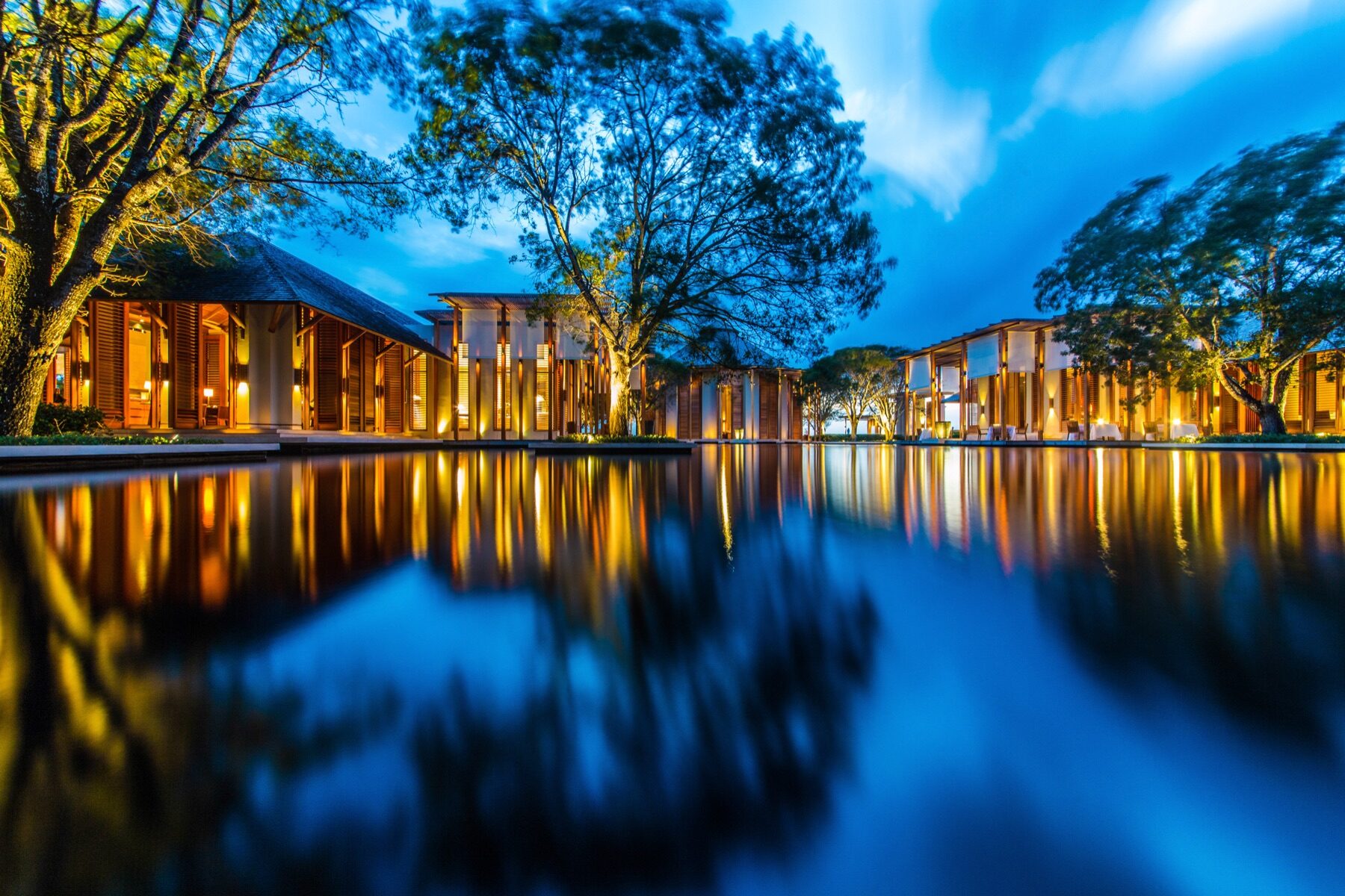 Wooden resort buildings reflected in a still lagoon pool at dusk