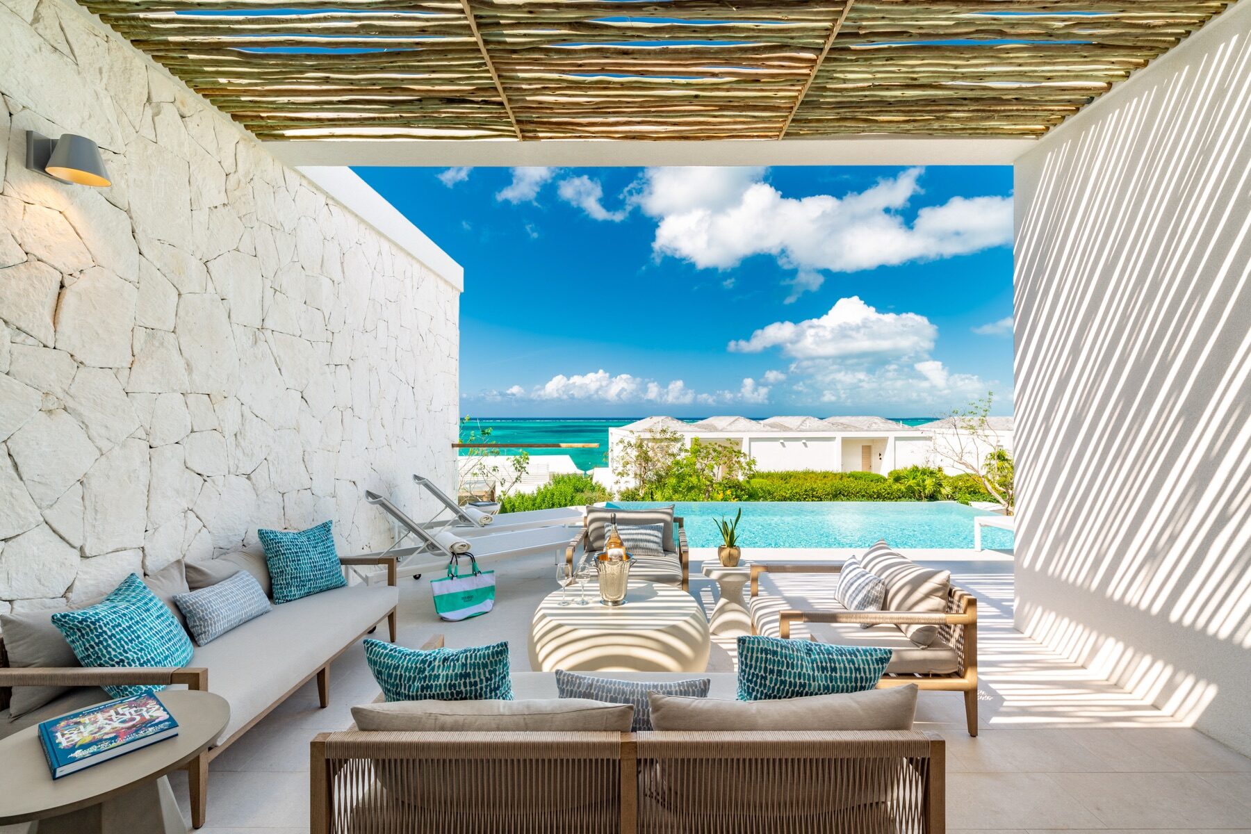 Covered patio lounge with woven furniture facing a resort infinity pool