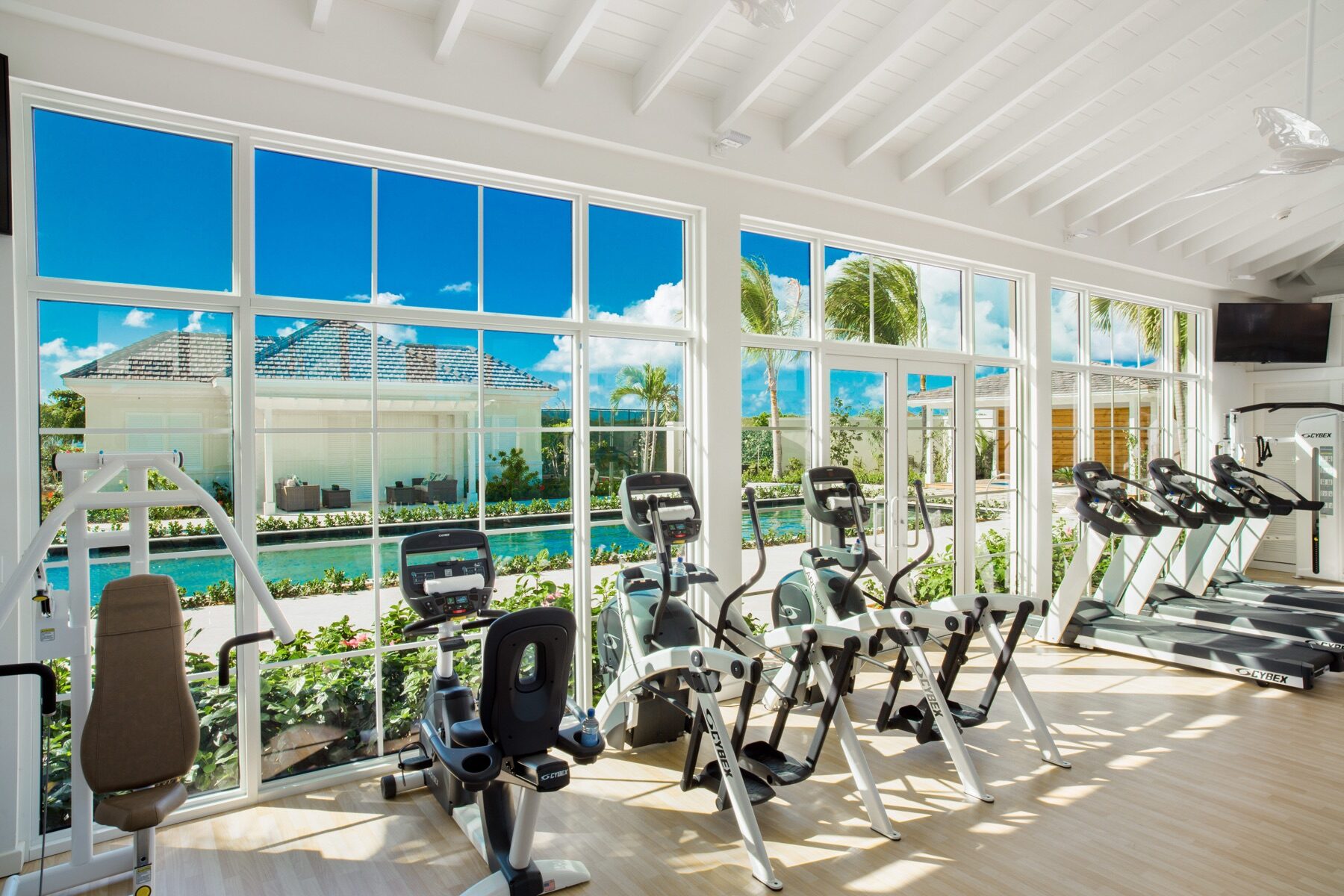 Resort fitness center with treadmills and elliptical machines facing floor to ceiling pool views