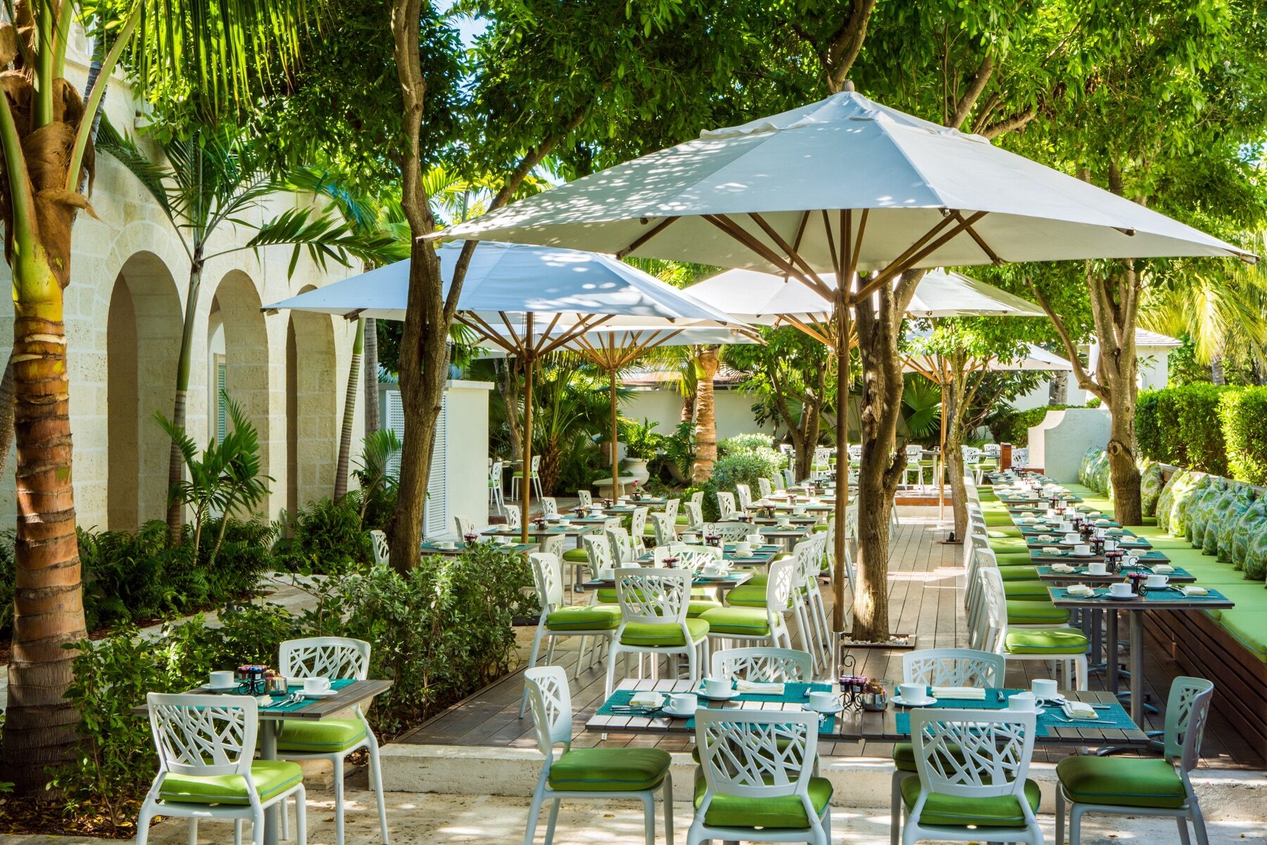 Garden terrace with dining tables shaded by white umbrellas among palm trees