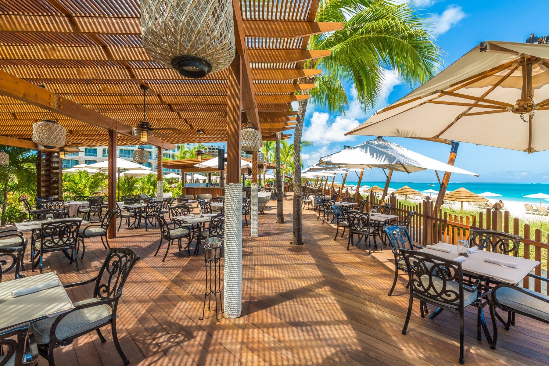 Beachfront restaurant deck with woven pendant lights and umbrellas near the shore
