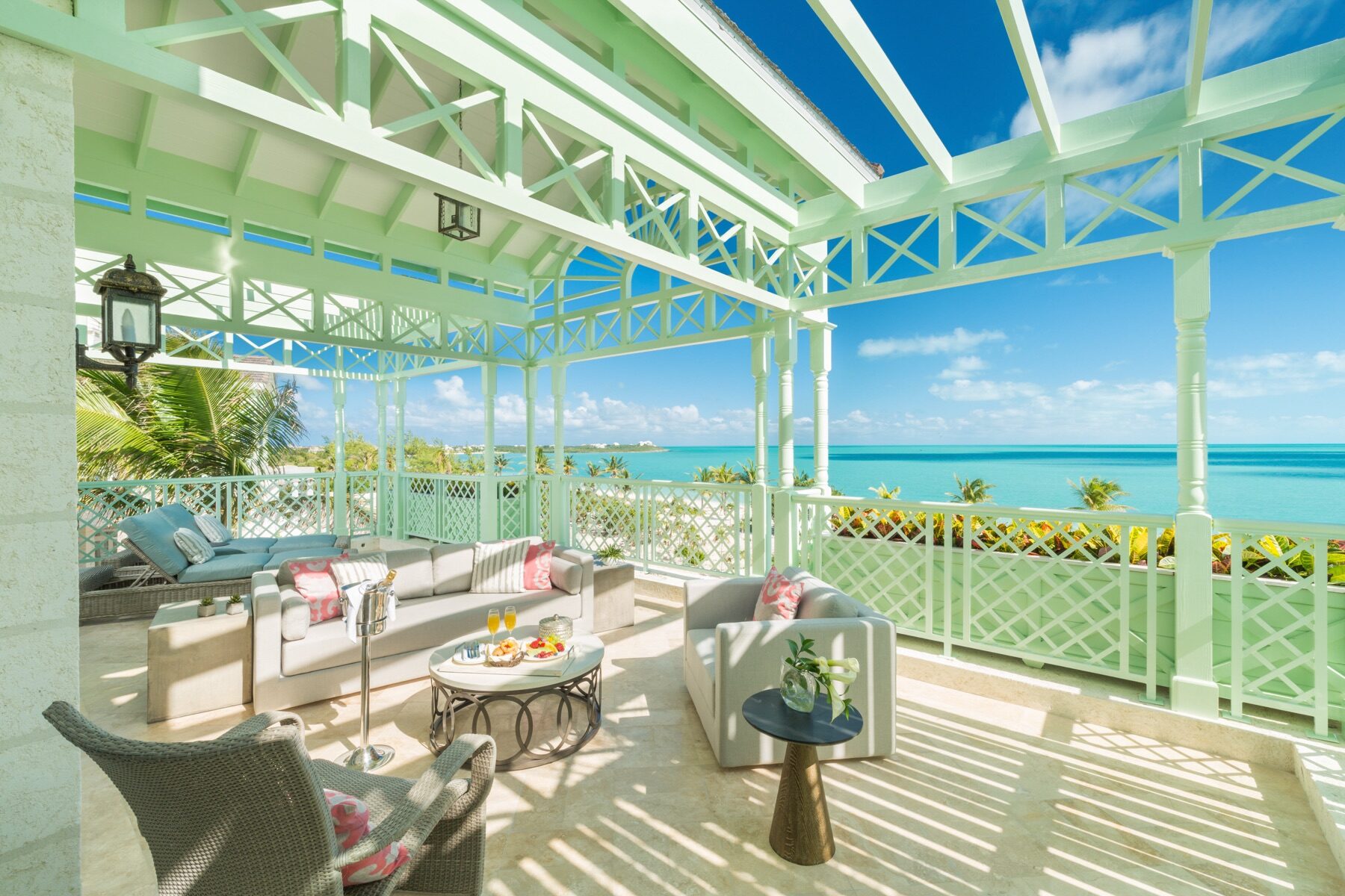 Pastel green veranda with lattice railings and wicker furniture overlooking the sea