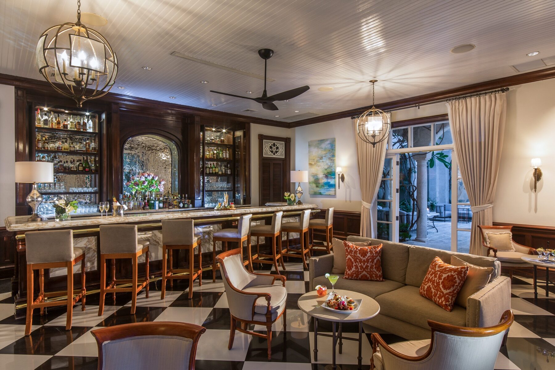 Dark wood hotel bar with glowing globe chandeliers and leather stools