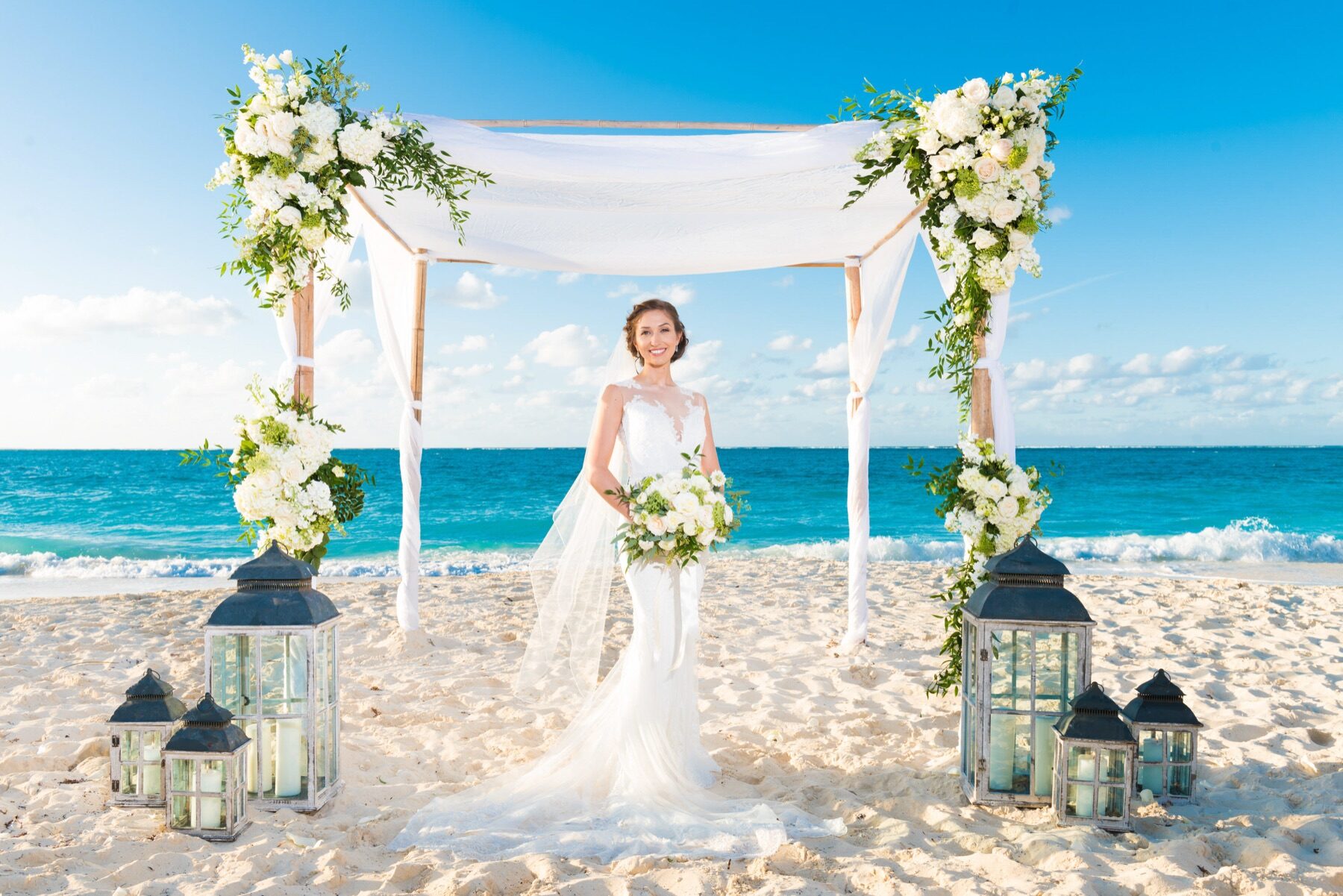 Bride holding a white bouquet under a floral canopy on a Turks and Caicos beach