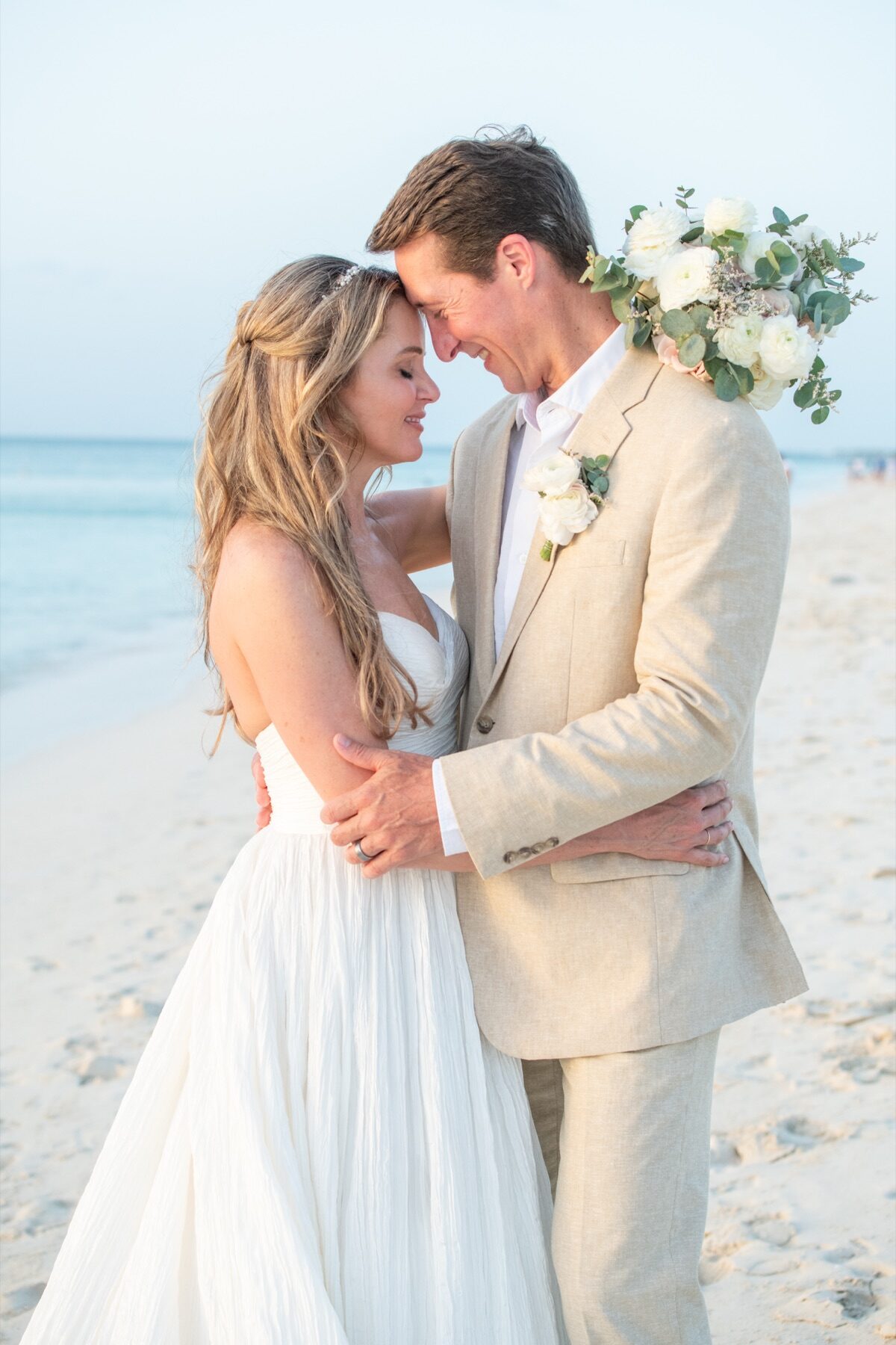 Bride and groom in tan suit pressing foreheads together on the shoreline