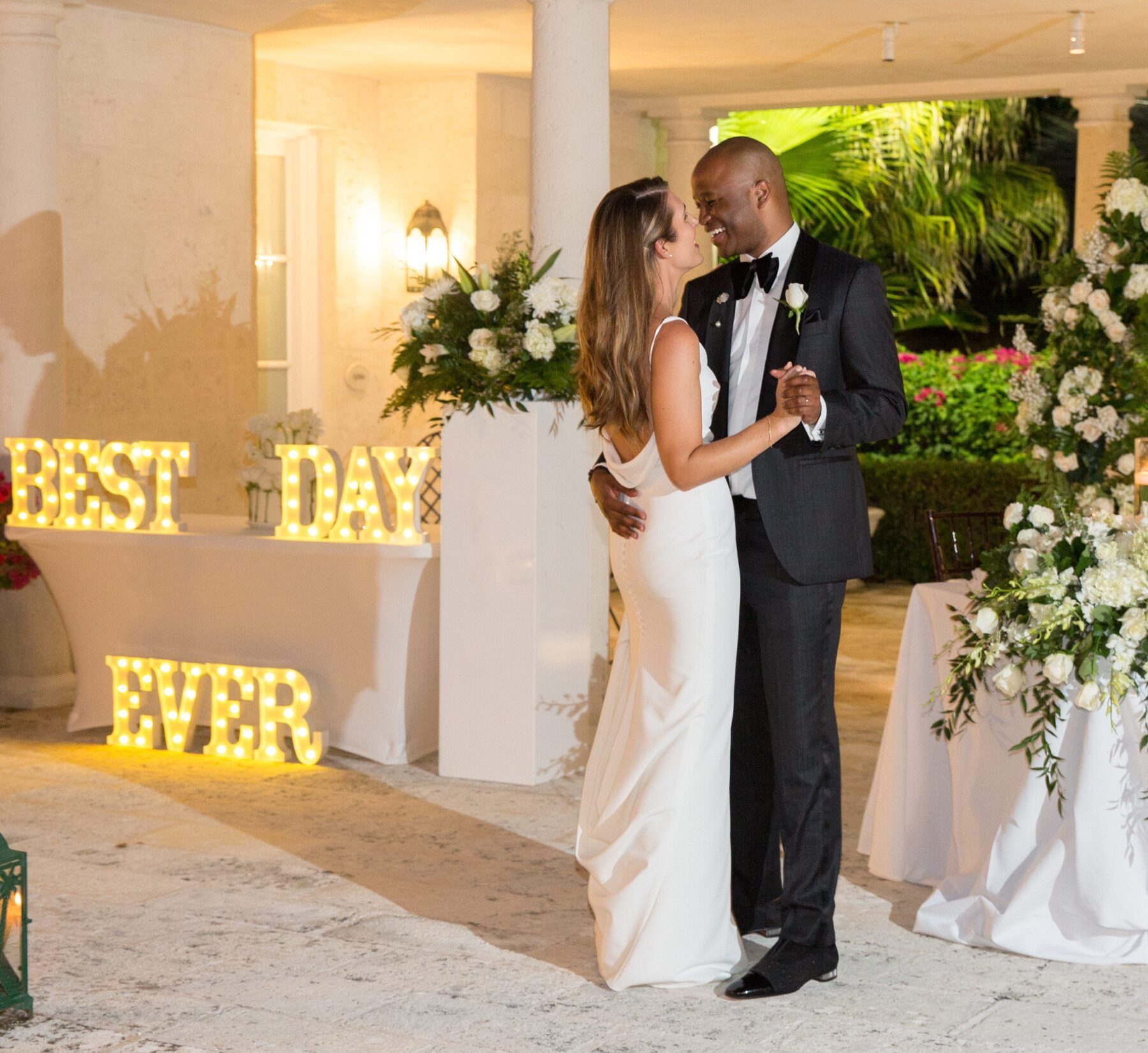 Bride and groom in tuxedo sharing a first dance beside glowing best day ever letters