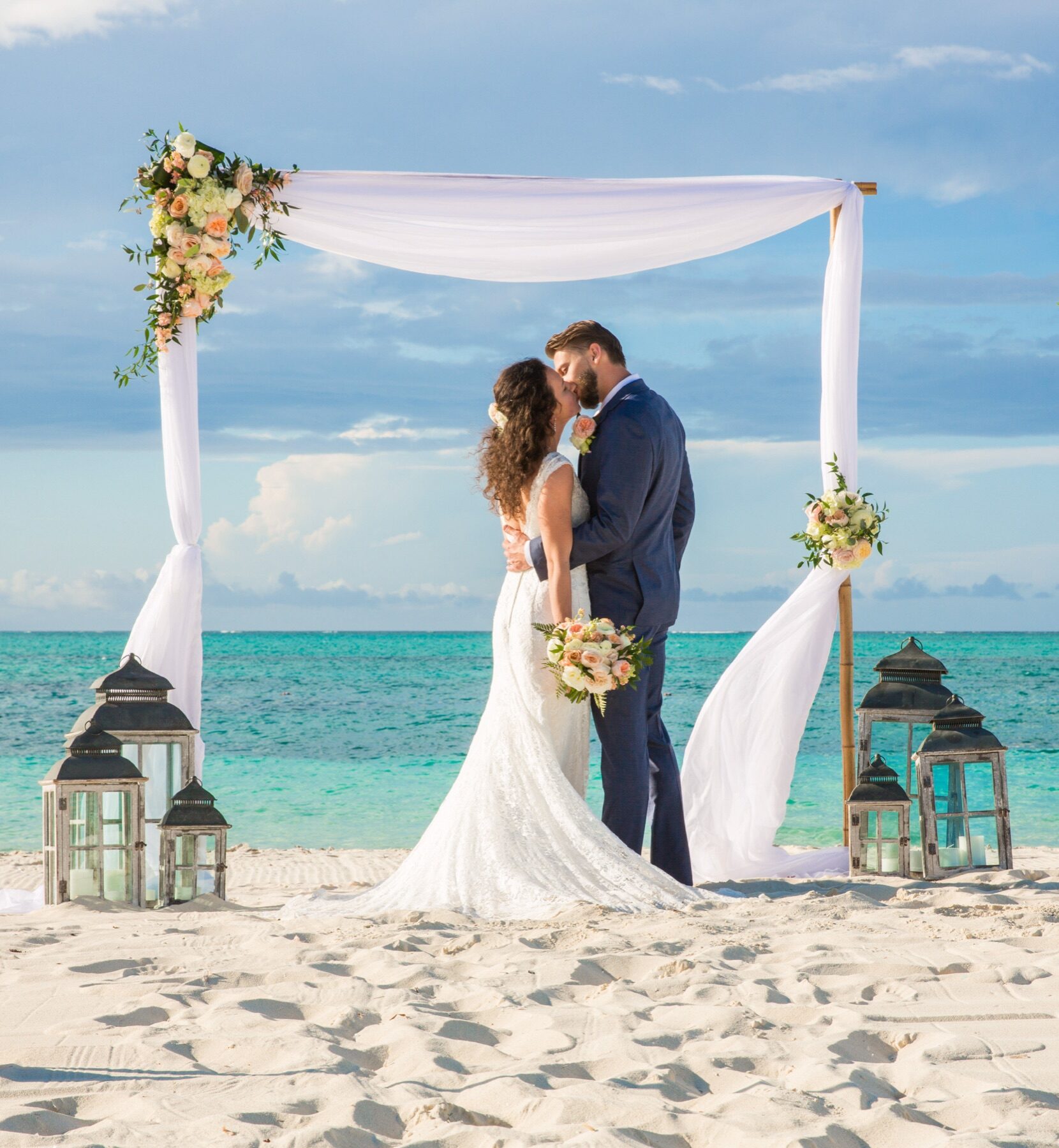 Bride and groom kissing beneath a white draped arbor in Turks and Caicos, flanked by lanterns