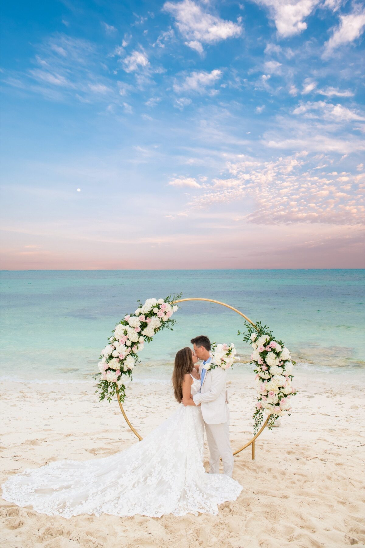 Couple kissing under a gold circular arch decorated with blush and white flowers