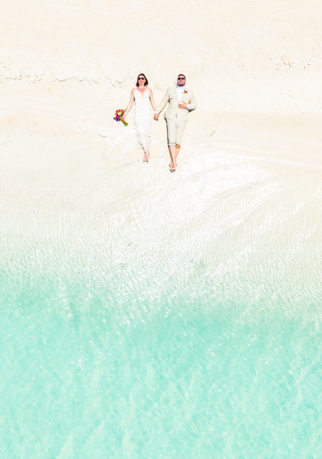 Aerial shot of bride and groom walking hand in hand along a Turks and Caicos sandbar