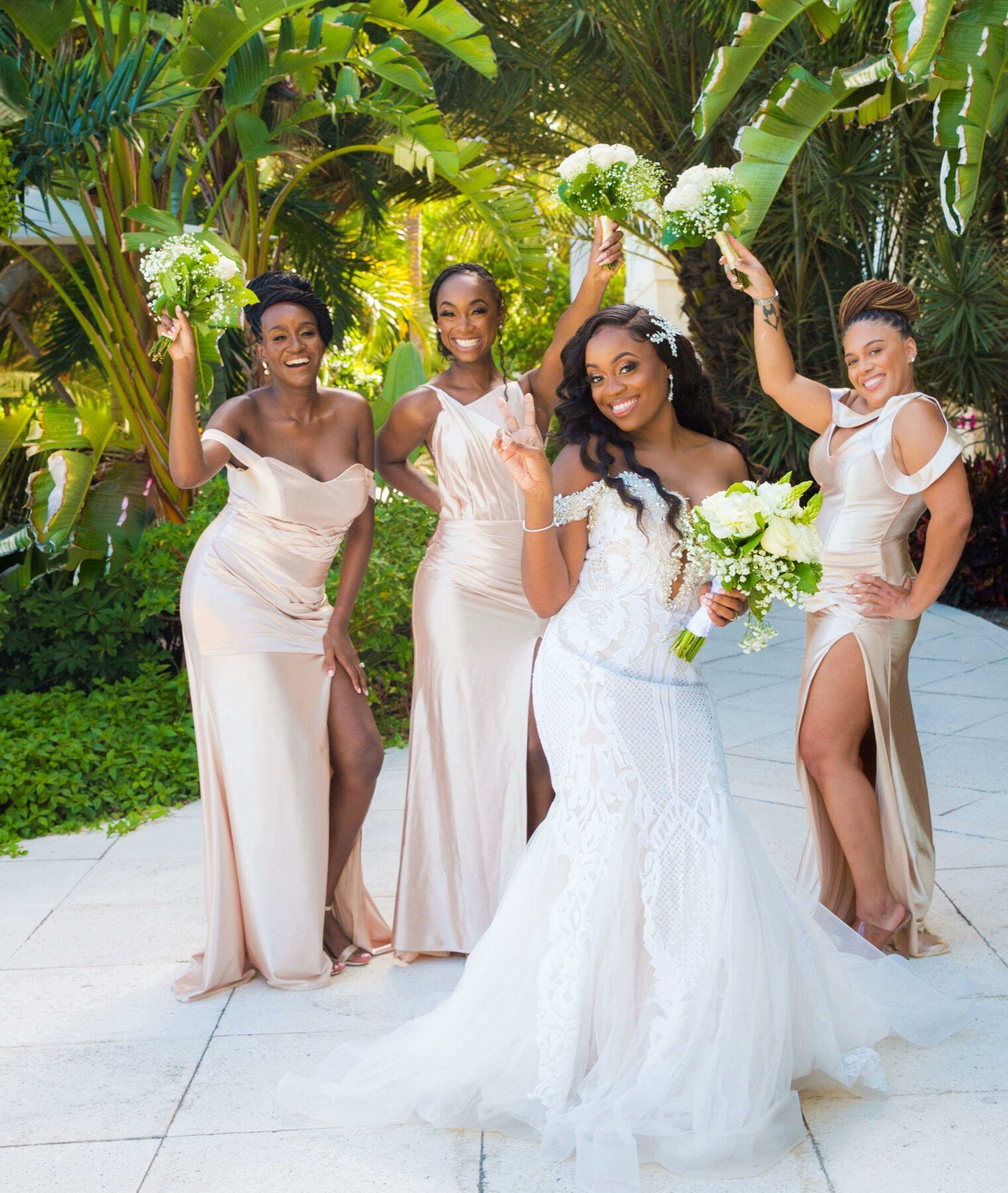 Three bridesmaids in champagne gowns cheering with bouquets raised beside the bride
