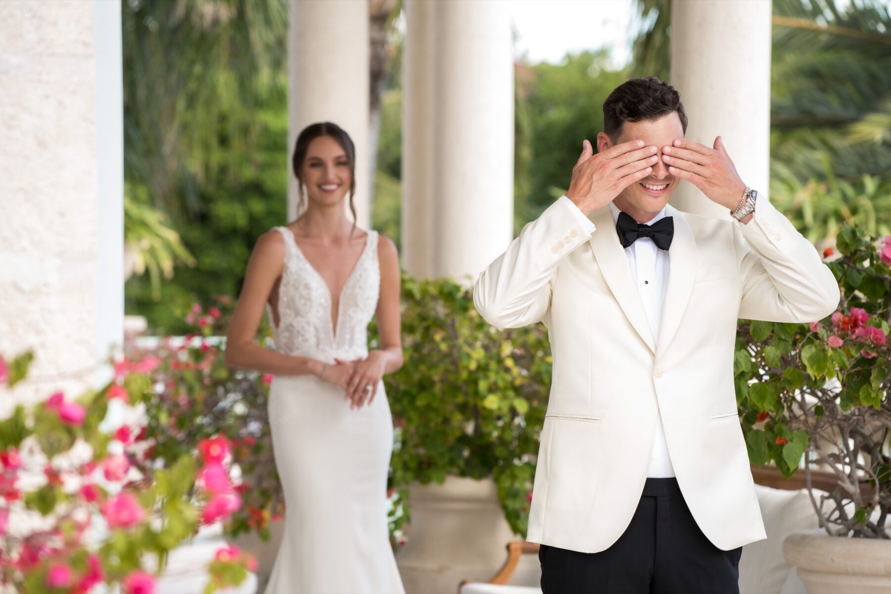 Groom covering his eyes before a first look as bride approaches under a colonnade