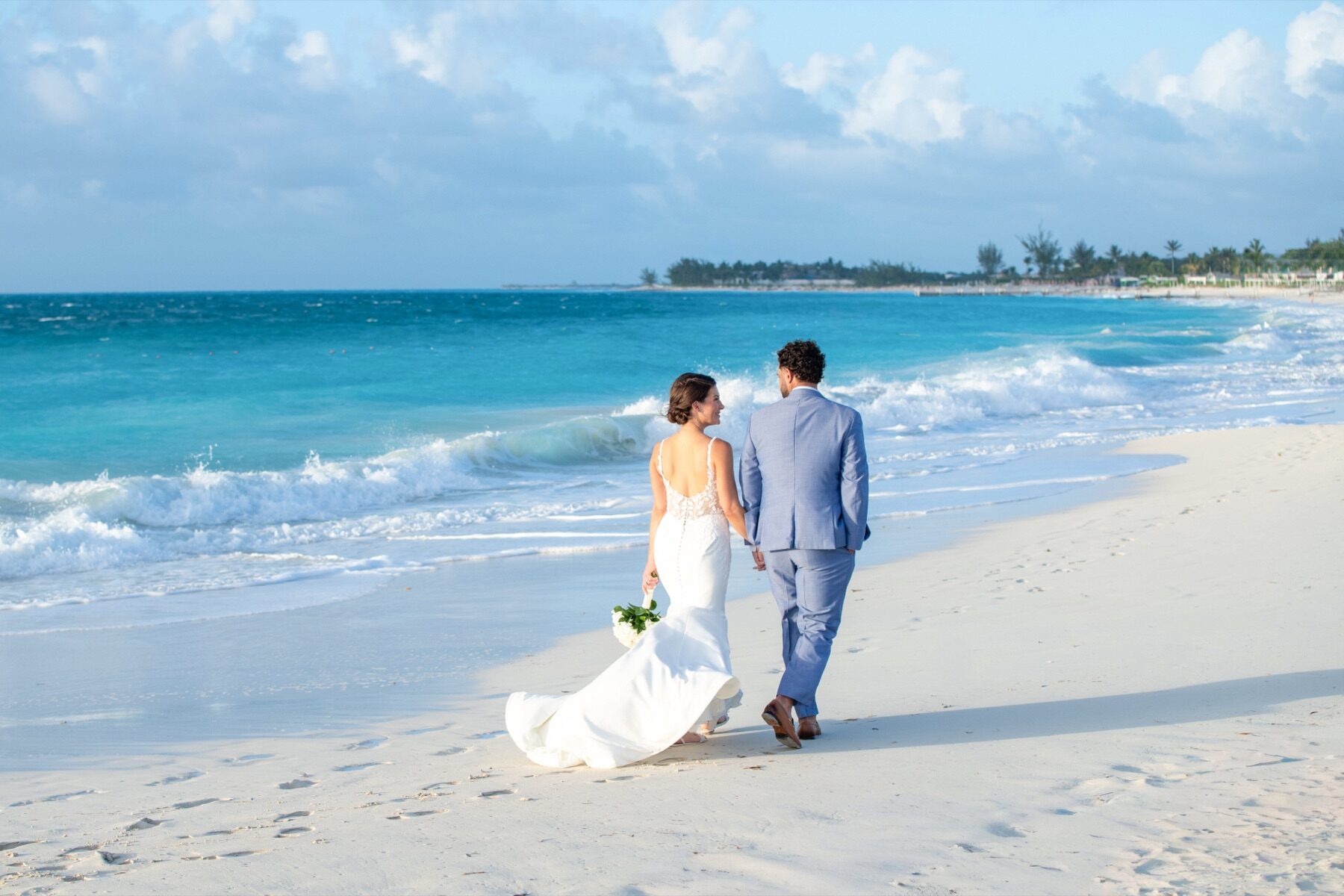 Bride and groom walking together along the shoreline with waves rolling in