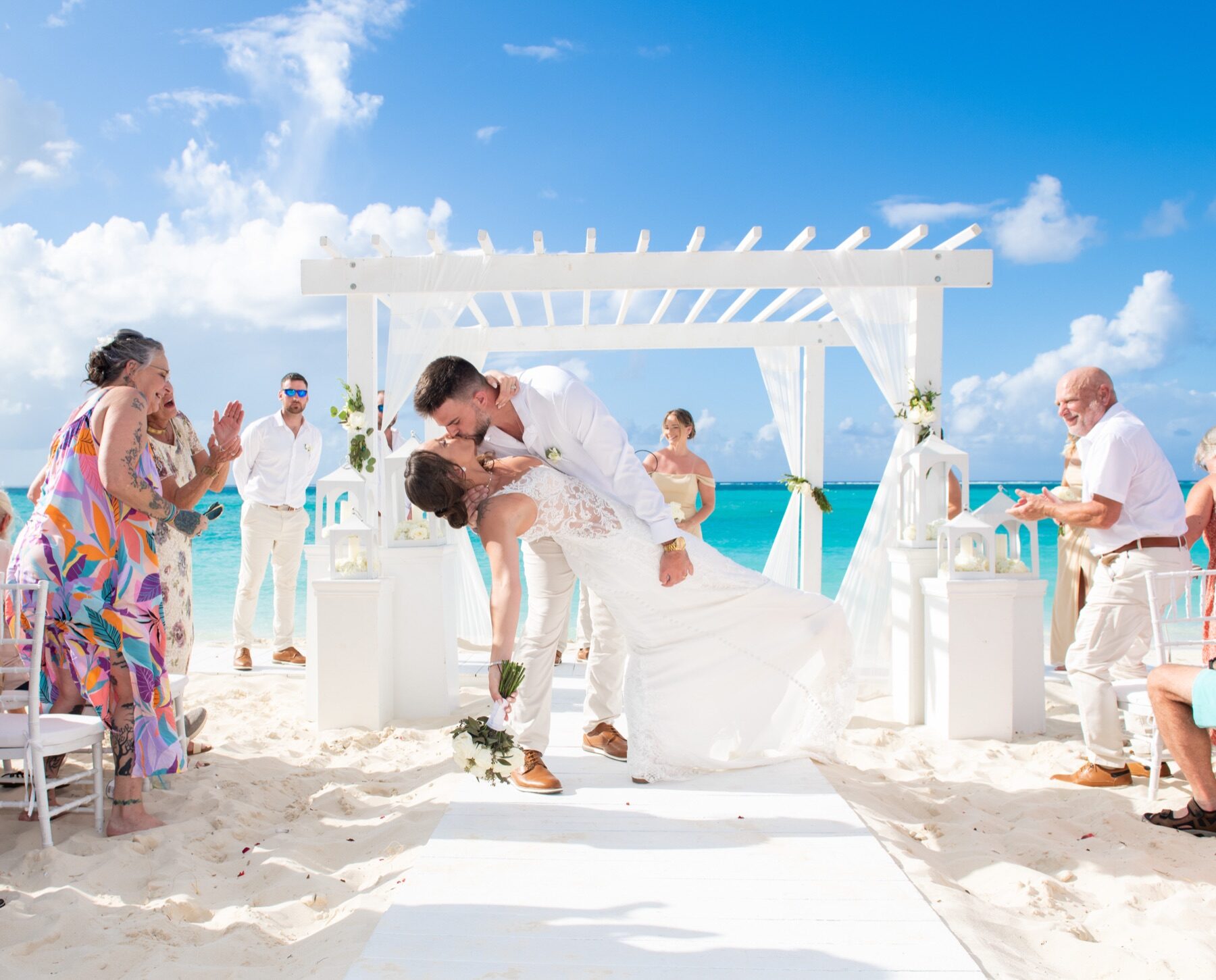 Groom dipping bride for a kiss under a white pergola as guests applaud