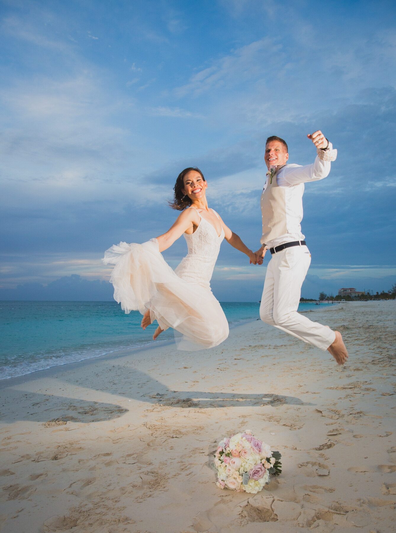 Bride and groom jumping in celebration on a Turks and Caicos beach at dusk