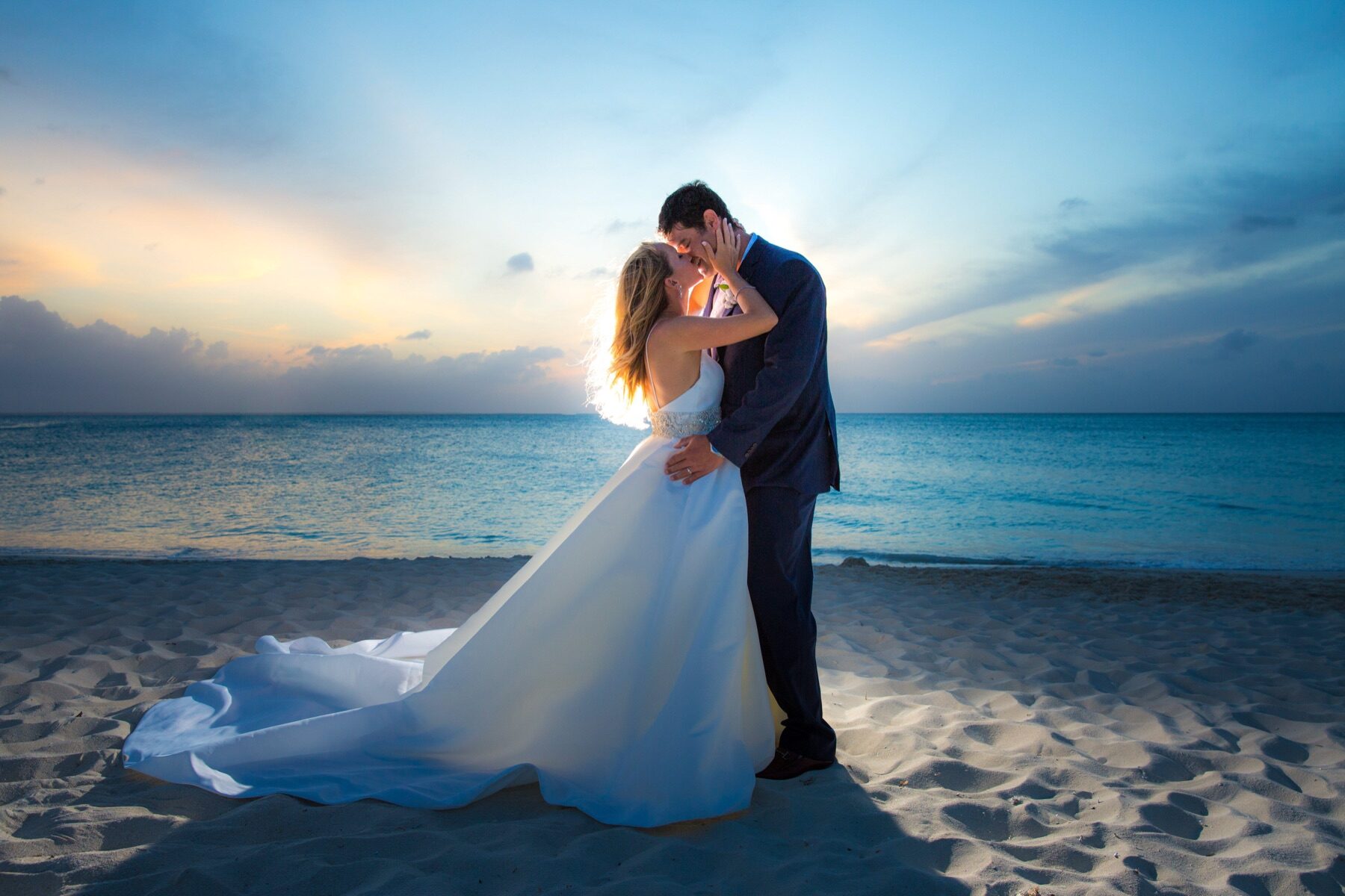 Silhouetted couple kissing on the beach as the sun sets behind them
