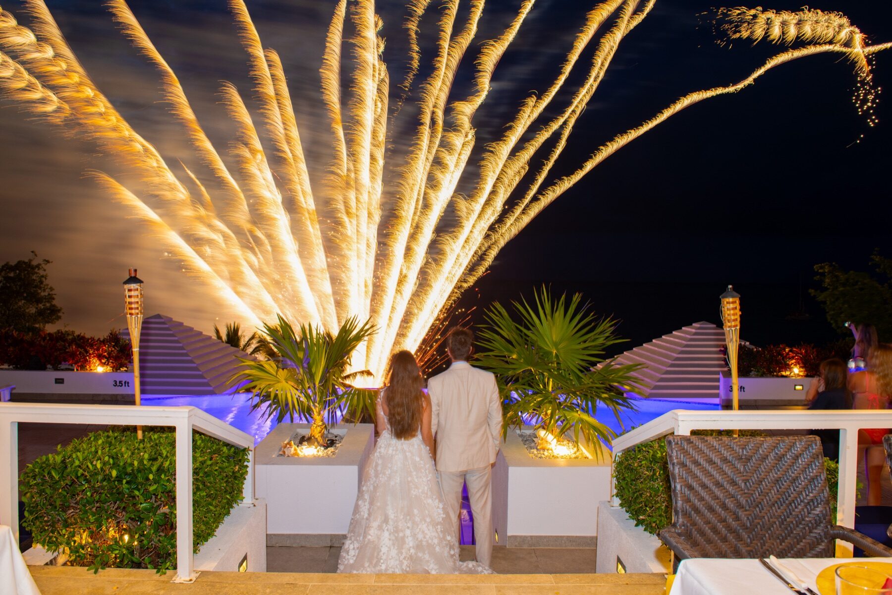 Bride and groom watching a burst of gold fireworks light up the Turks and Caicos night sky